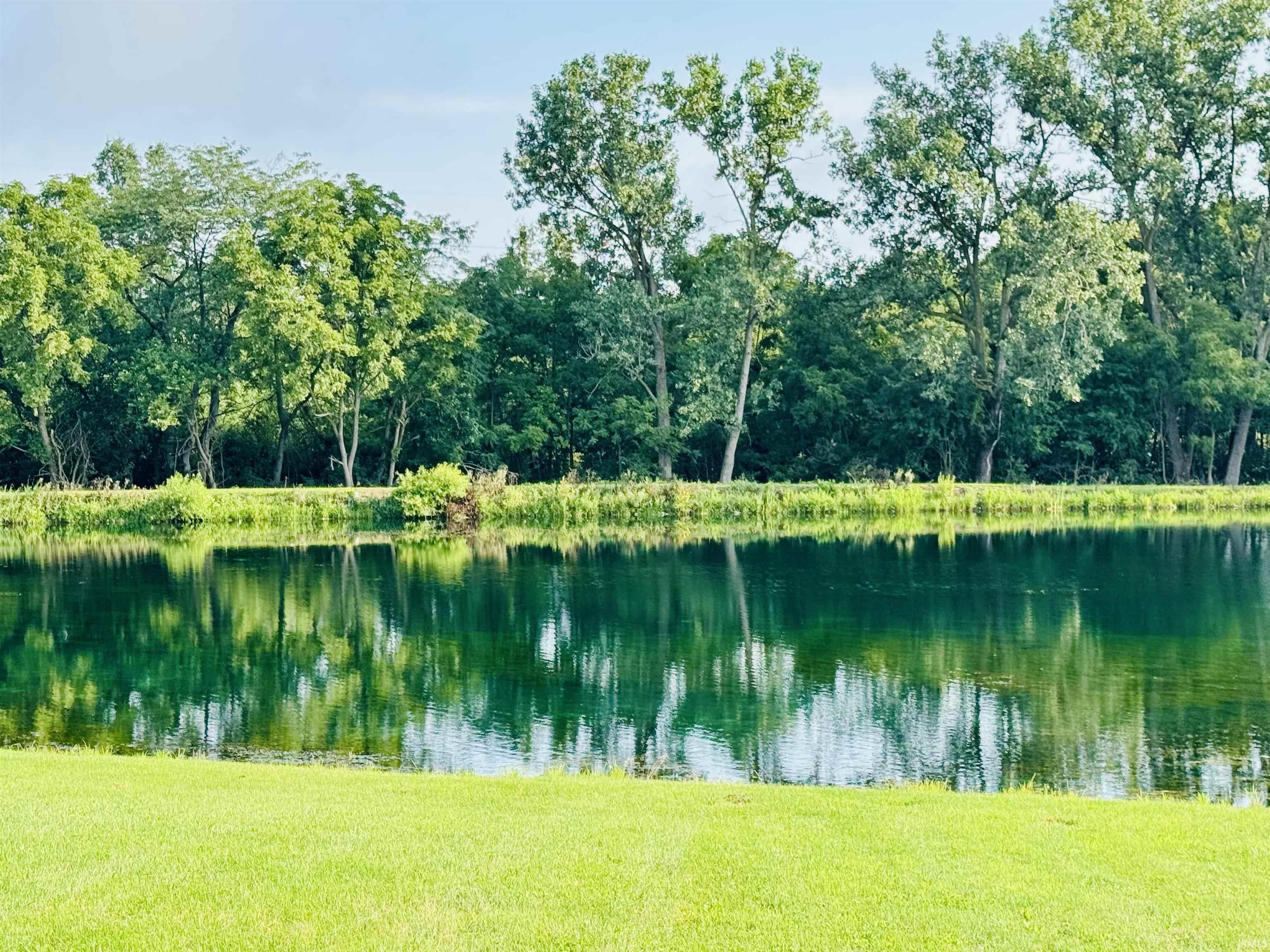 Manicured lawn fronting a reflective body of water with mature trees