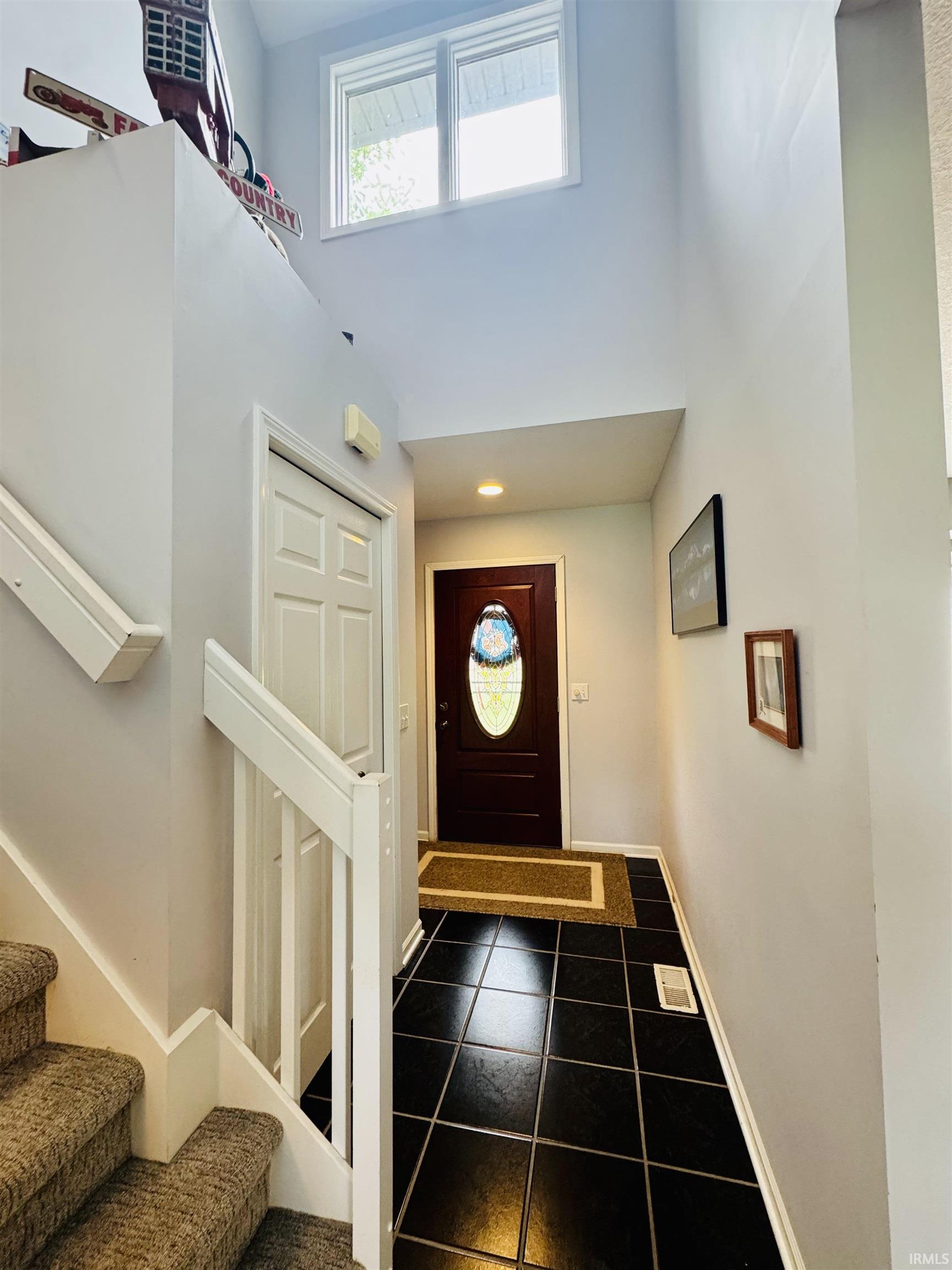 Two-story entry foyer with a dark wood-finish door, oval-shaped decorative glass insert, and black tile flooring