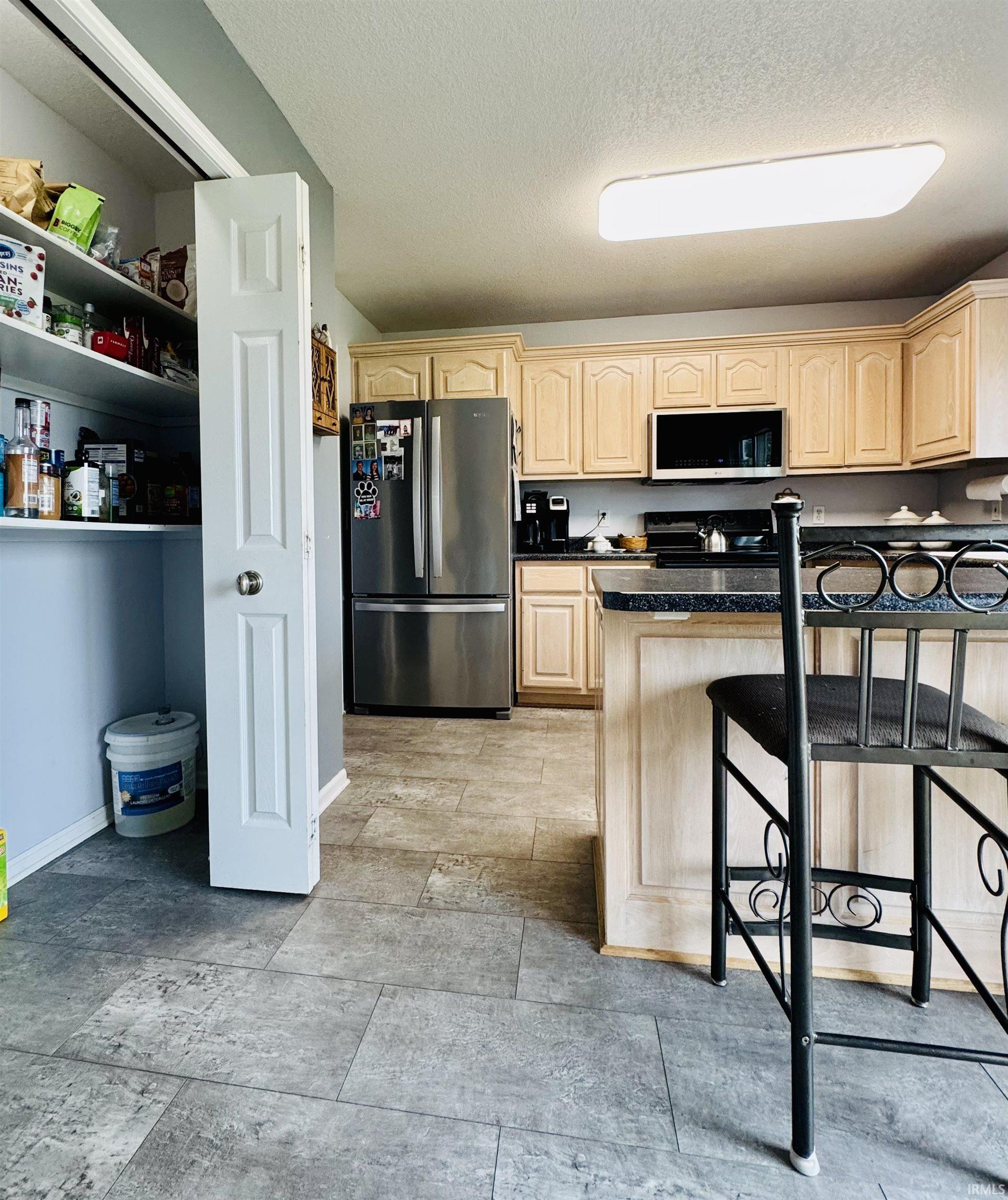 Kitchen featuring stainless steel appliances, light wood-finish cabinetry, and dark countertops