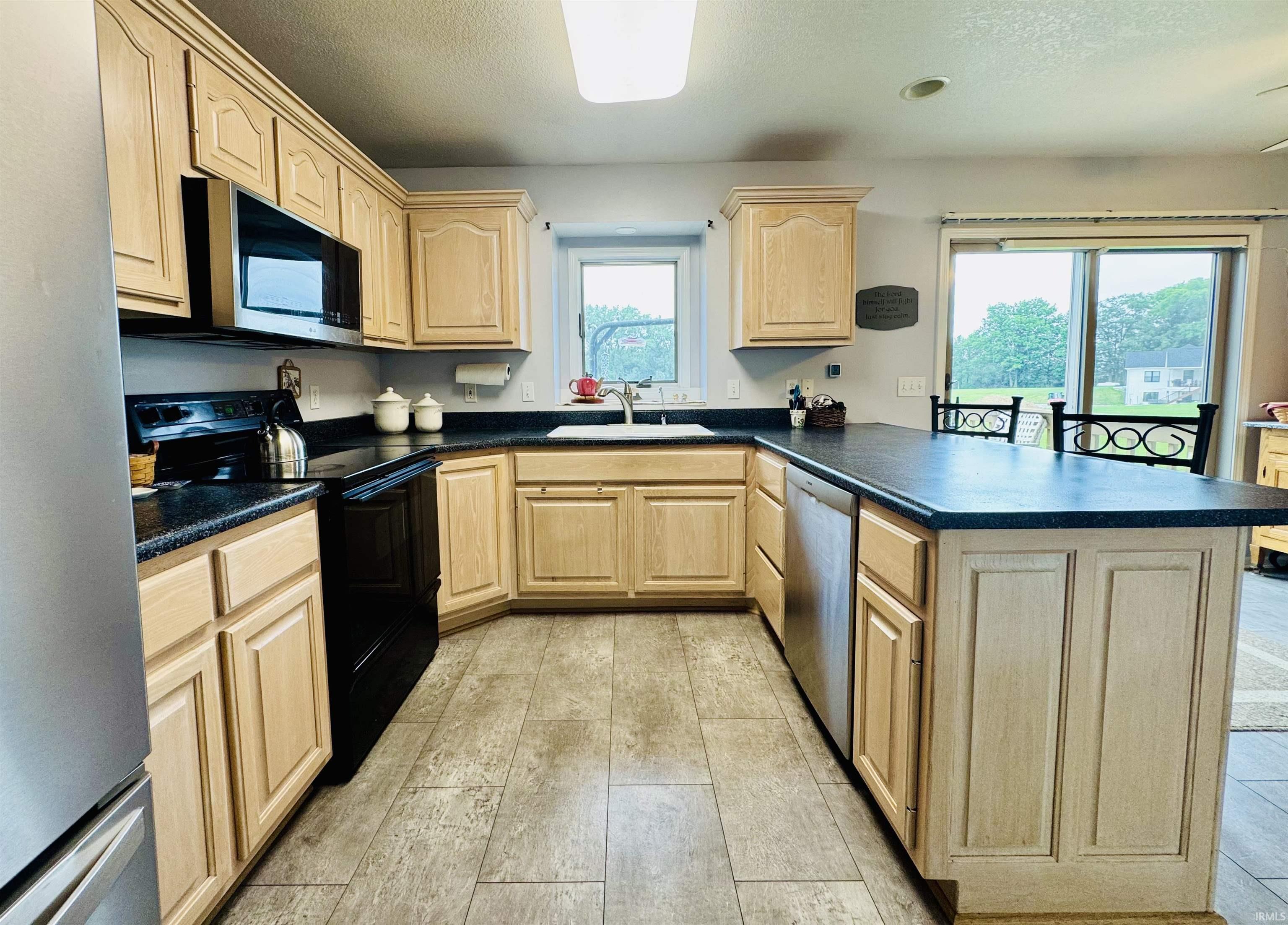 Kitchen featuring wood-finish cabinetry, dark countertops, built-in stainless steel microwave, and tile-finish flooring
