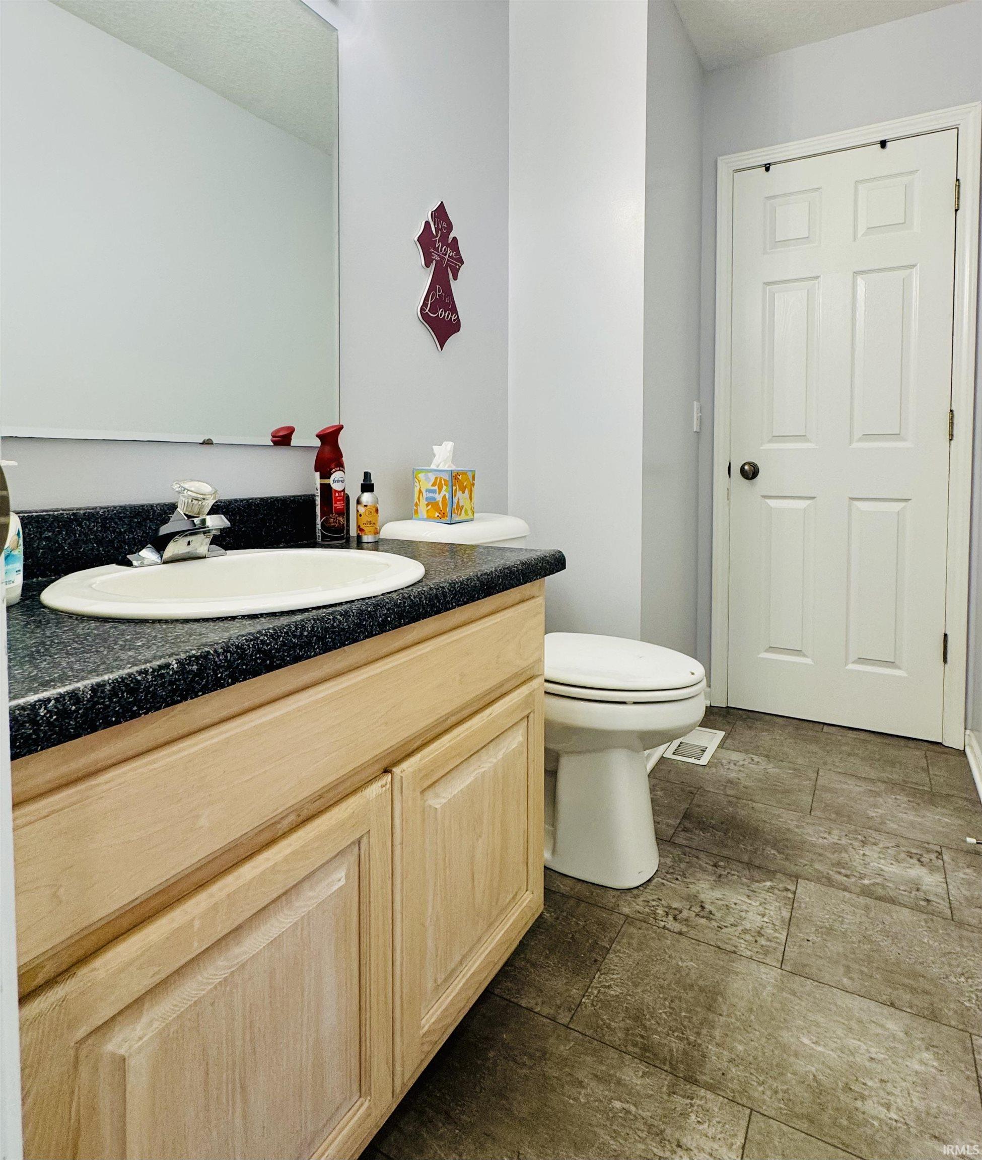 Neutral-toned tile flooring, light wood-finish vanity with an integrated sink, dark countertop, and a paneled interior door