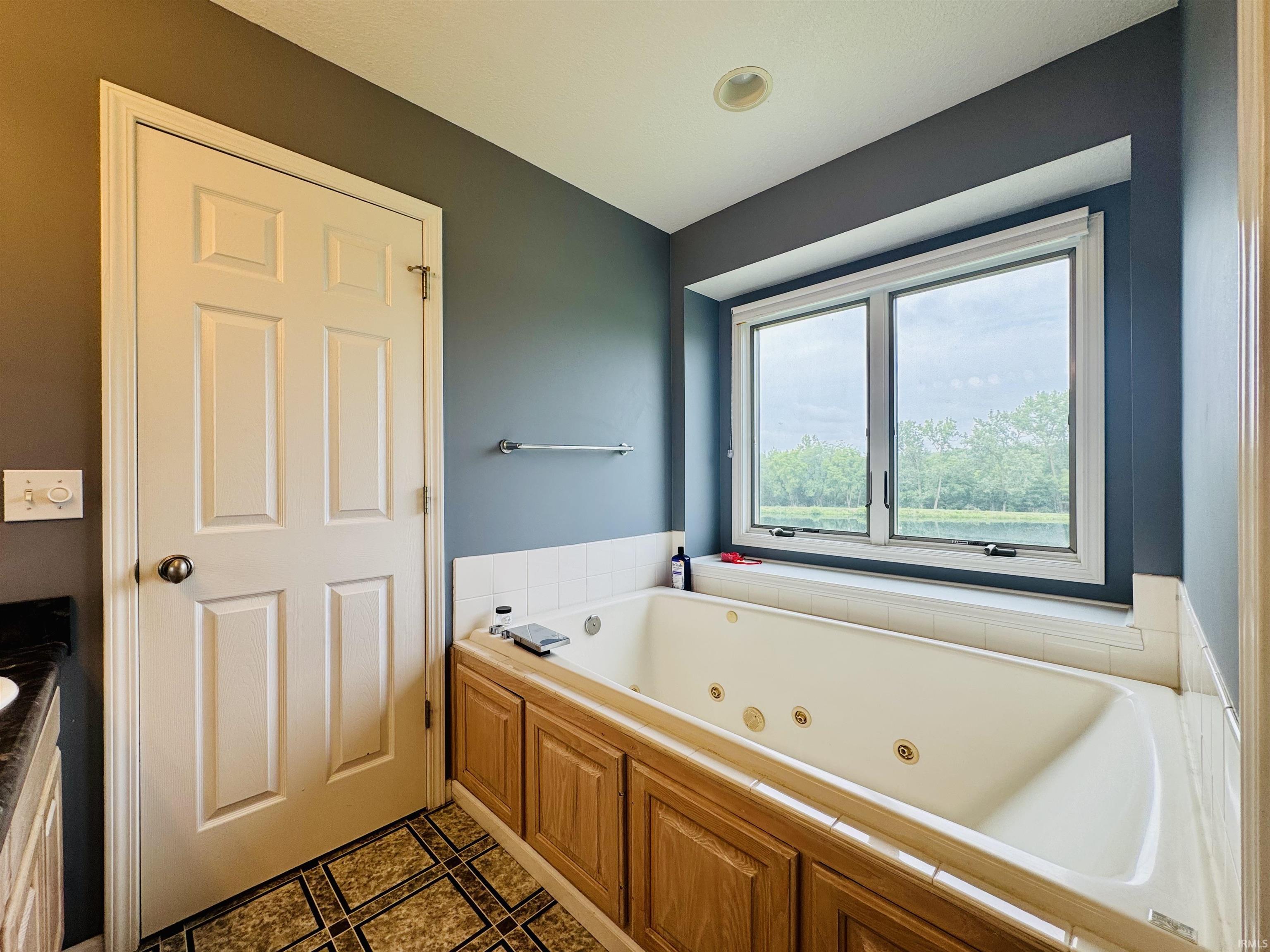 Jetted soaking tub with a tiled surround, wood-finish cabinetry, and a large window