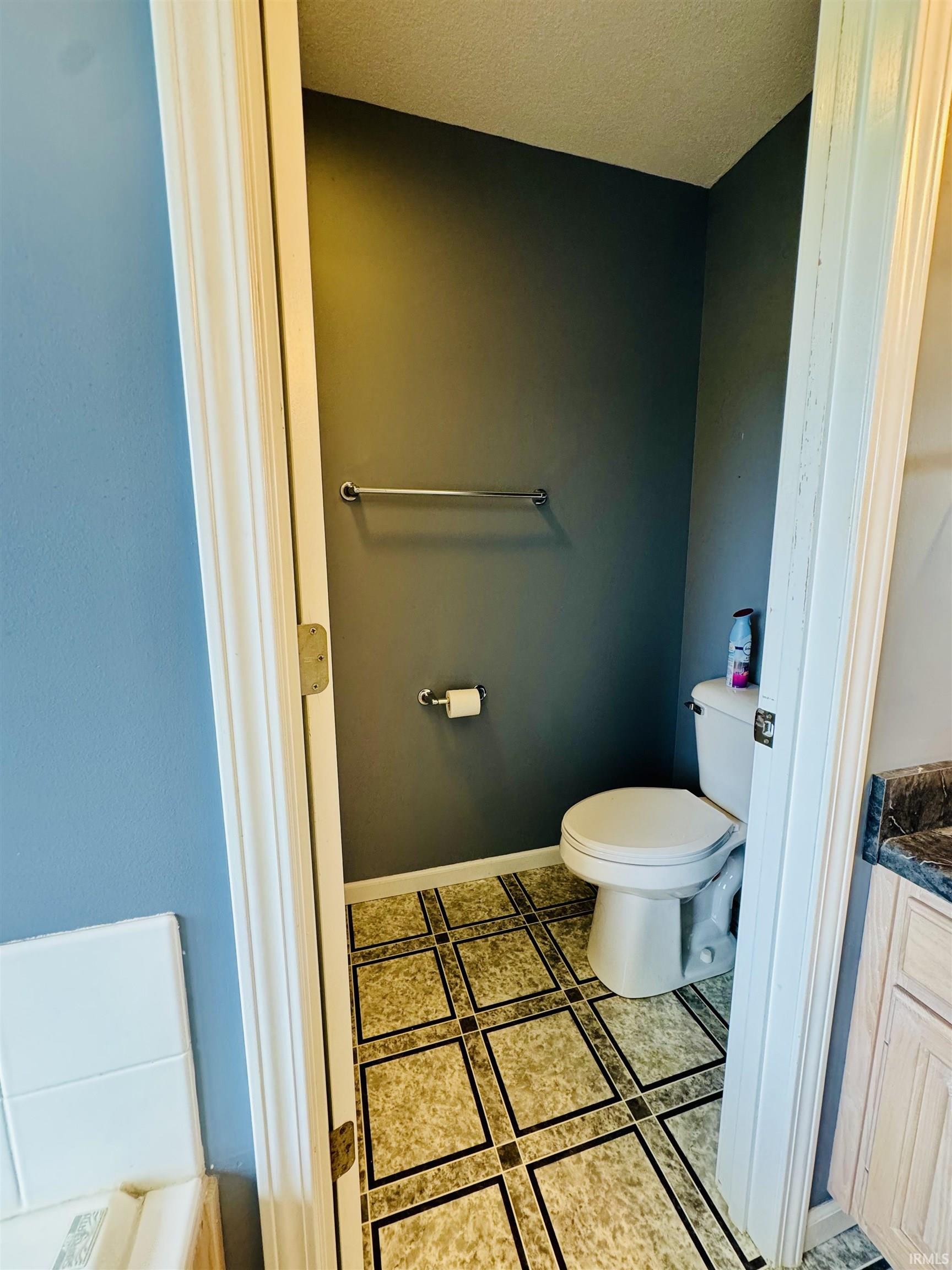 Bathroom featuring patterned tile flooring, a white toilet, and a chrome towel bar