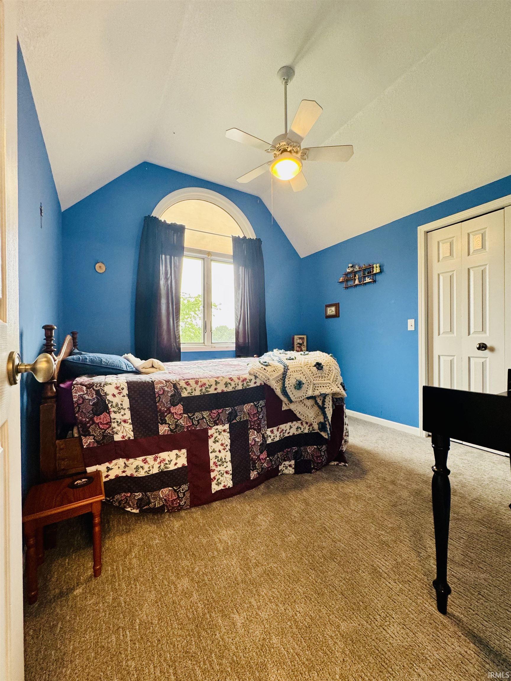 Vaulted ceiling with a ceiling fan, arched window, and carpeted flooring