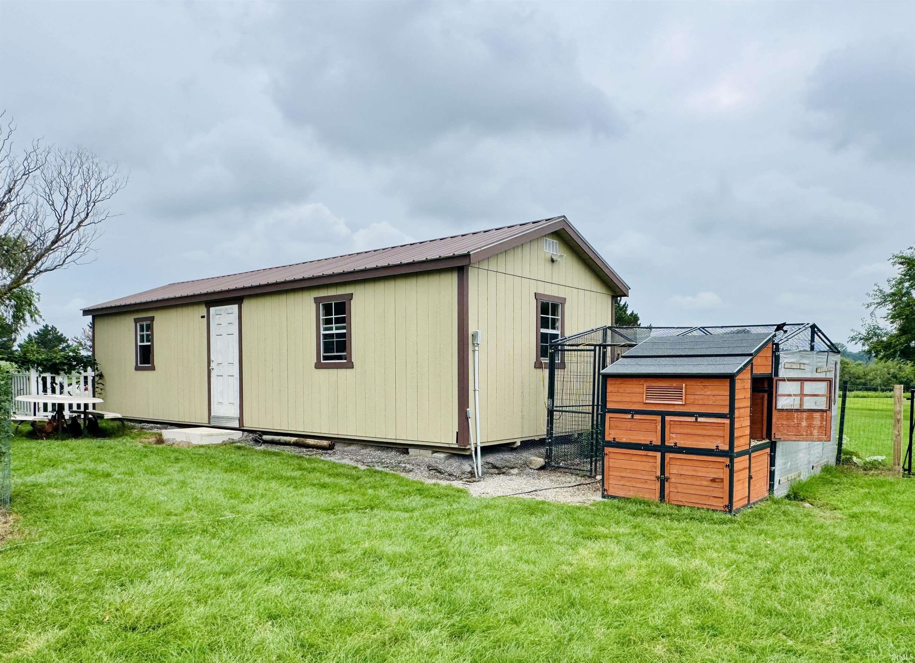 Detached structure with vertical siding and a brown metal roof, featuring a white entry door and multiple windows