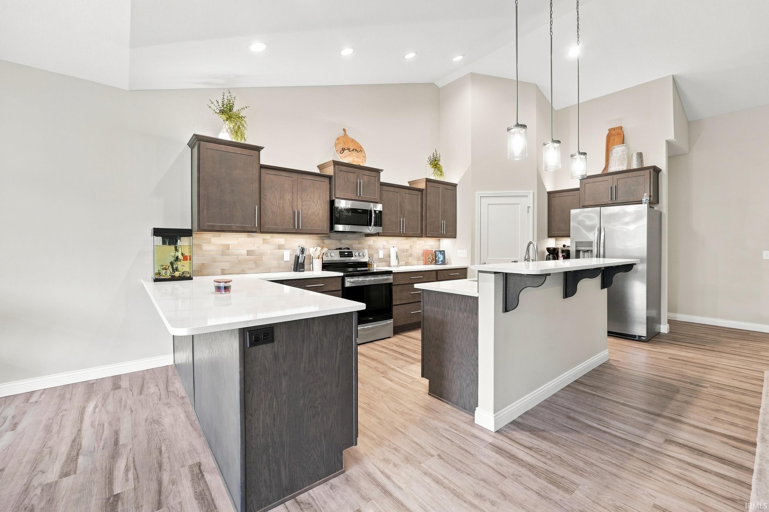 Kitchen featuring vaulted ceilings, wood-finish flooring, dark wood cabinetry, white countertops, and stainless steel appliances