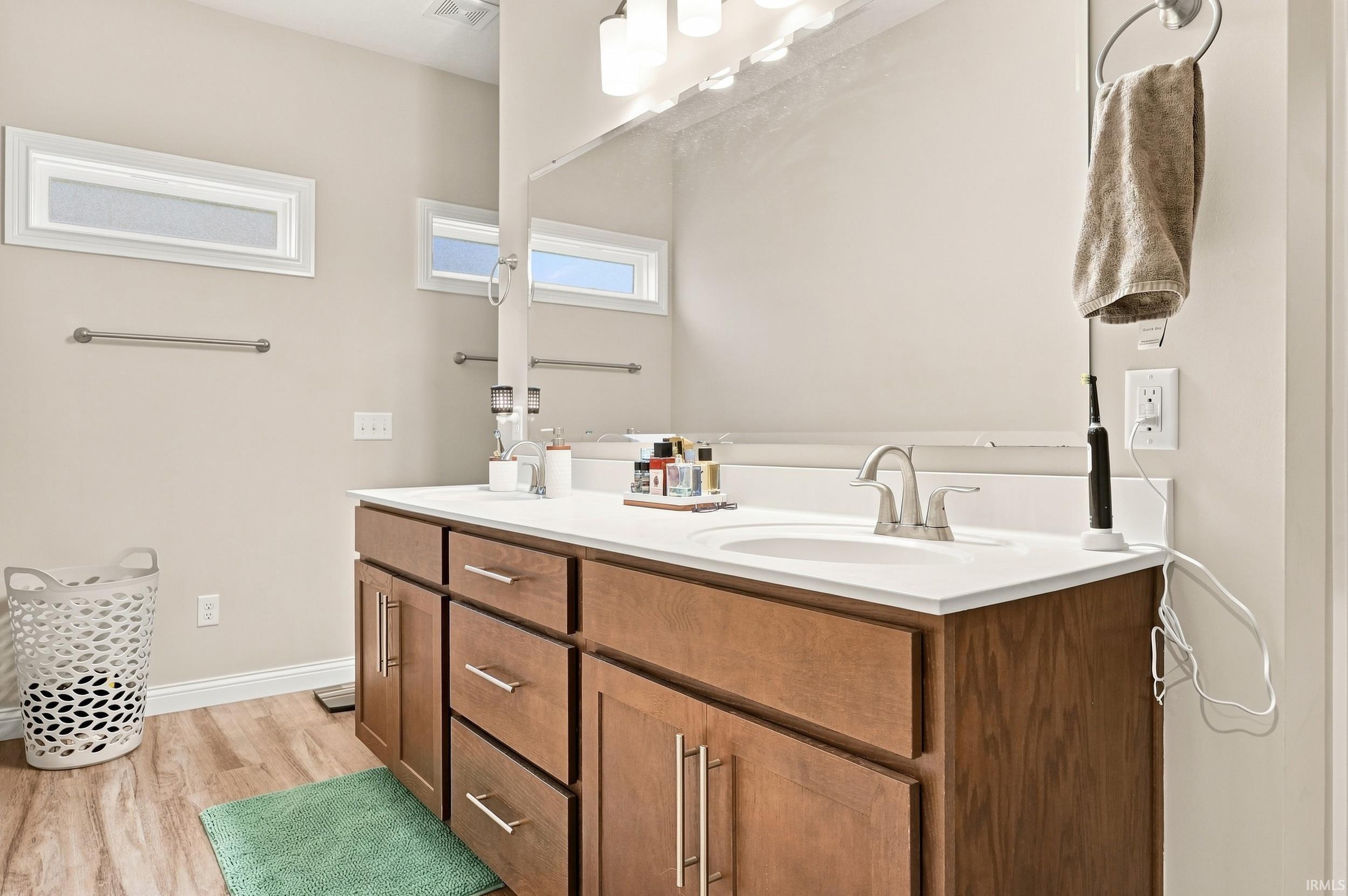 Wood-finish flooring, dual windows, integrated vanity lighting, and a double vanity with a single basin