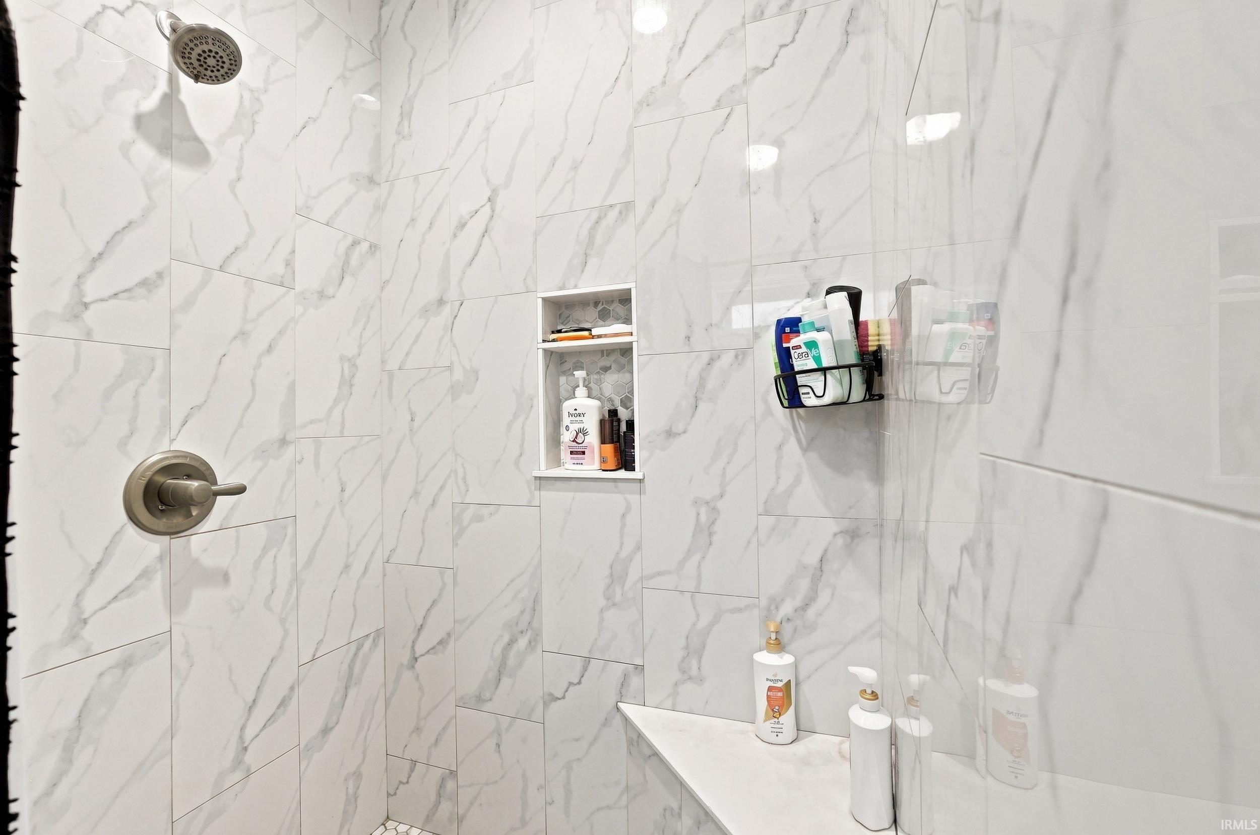 Shower with large format marble-look wall tiles, brushed nickel shower head and control, built-in shower niche, and integrated shower bench