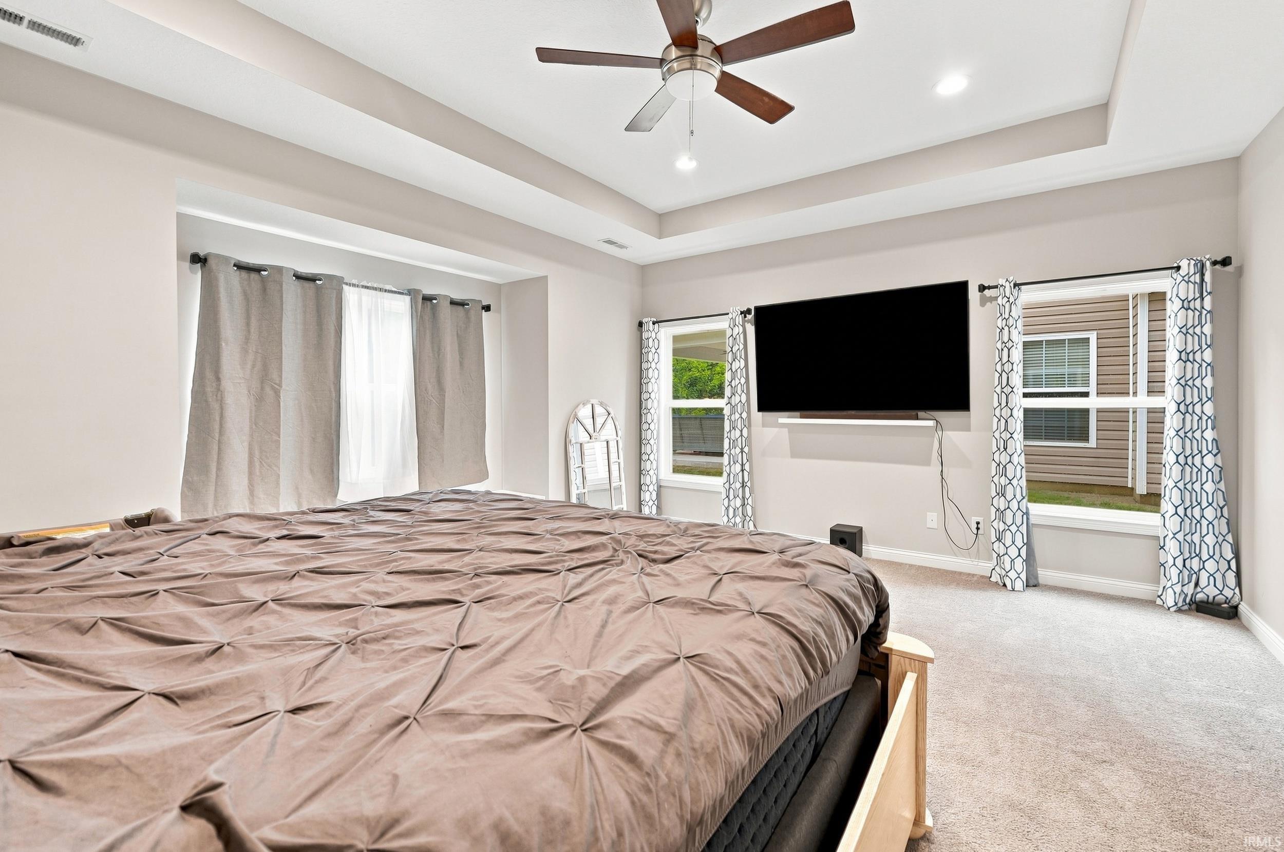 Tray ceiling with recessed lighting, ceiling fan with wood-finish blades, multiple windows, and carpet flooring