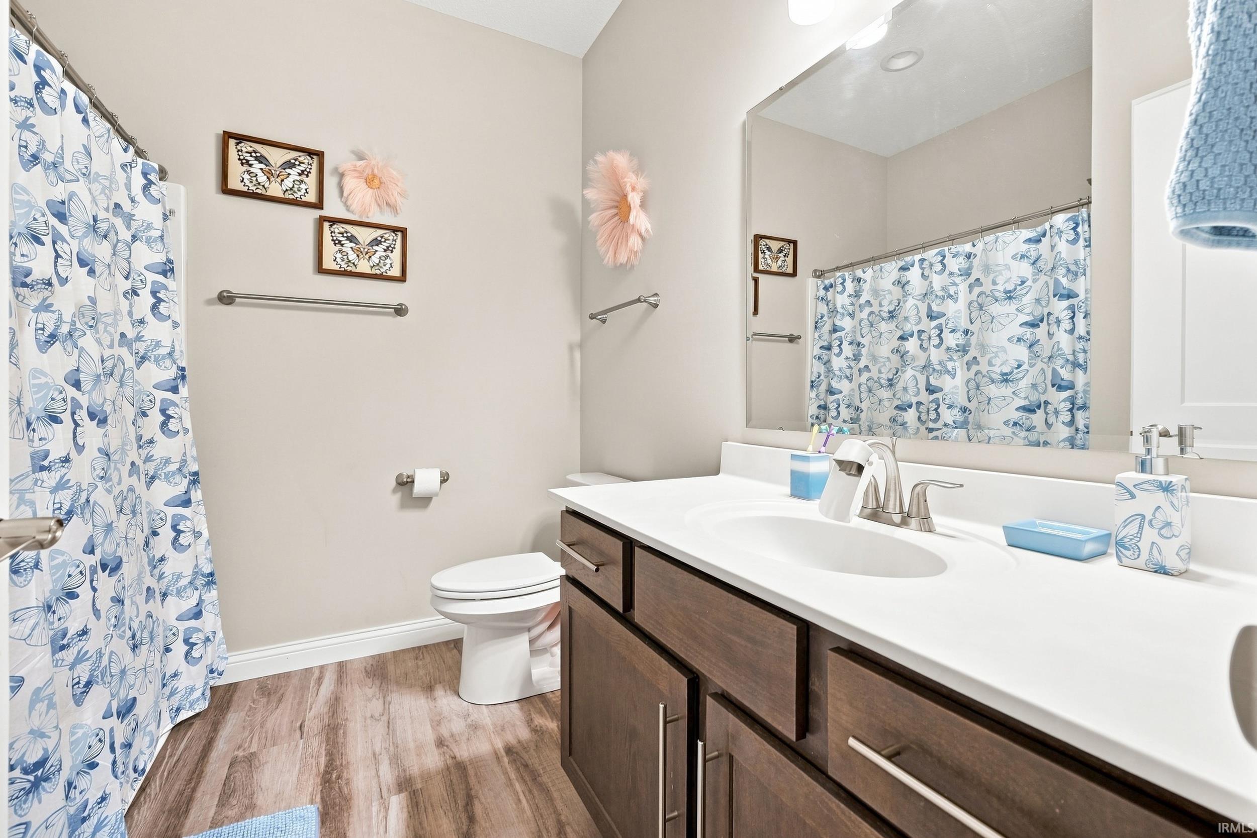 Bathroom featuring a wood-finish floor, single vanity with white countertop, integrated sink, and brushed nickel fixtures