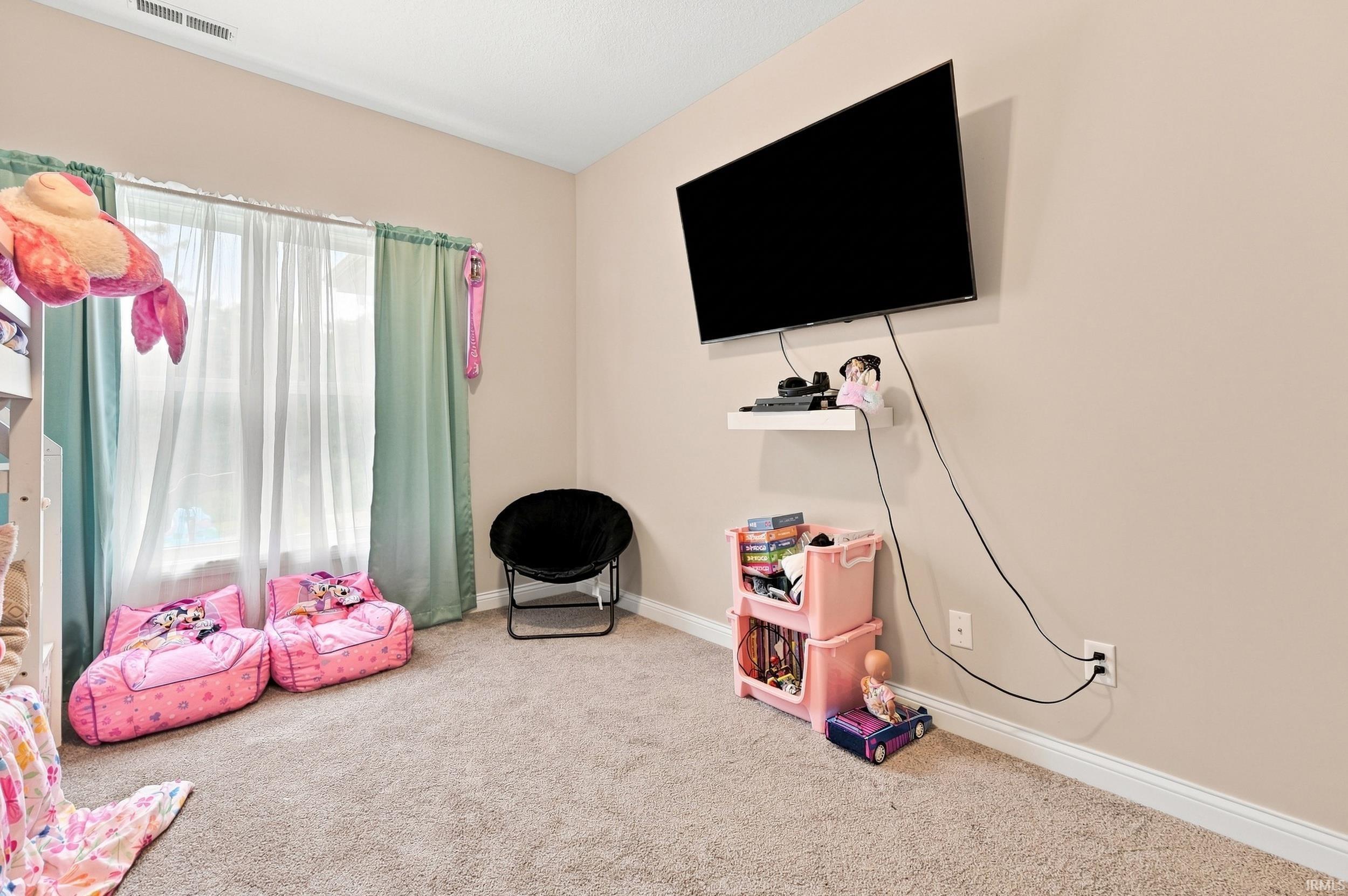 Wall-mounted television with a white floating shelf, carpet flooring, and a window with curtain rods