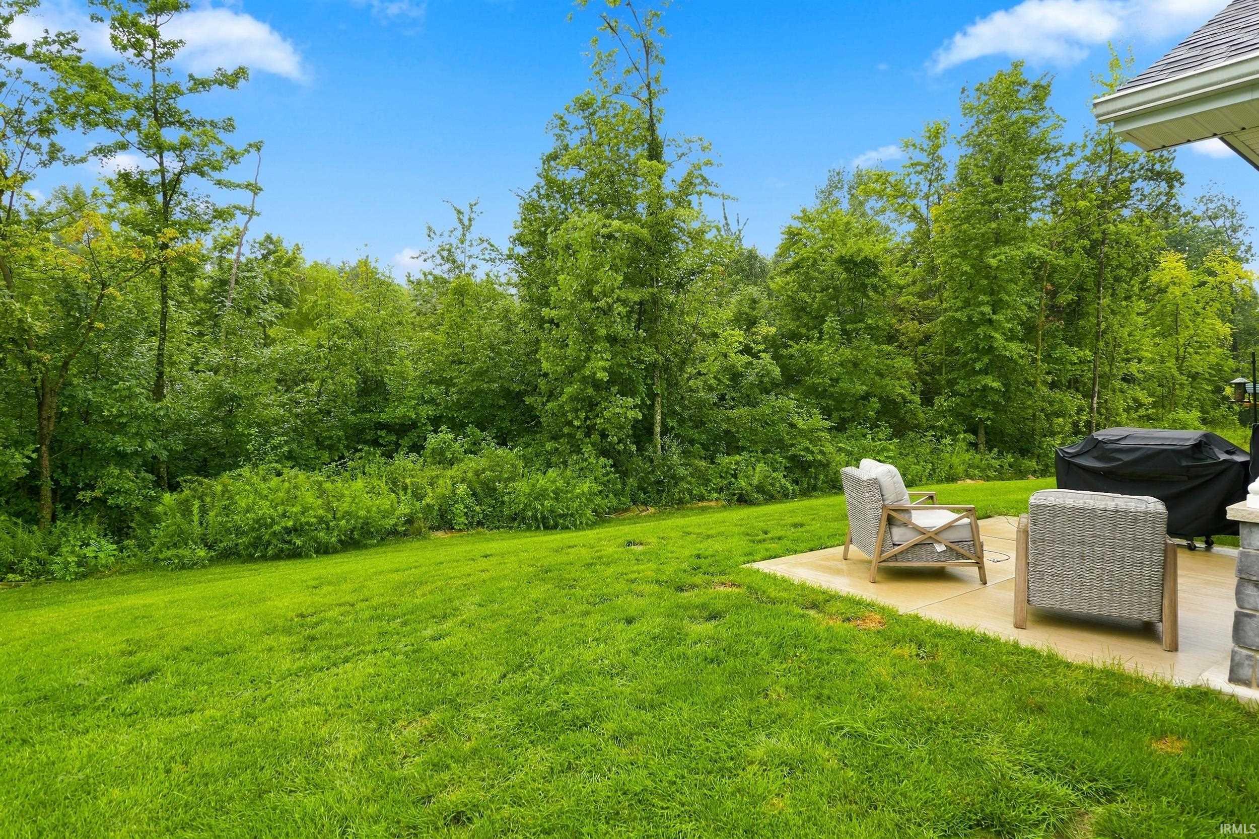Expansive green lawn with a concrete patio, surrounded by mature trees, featuring a gutter system