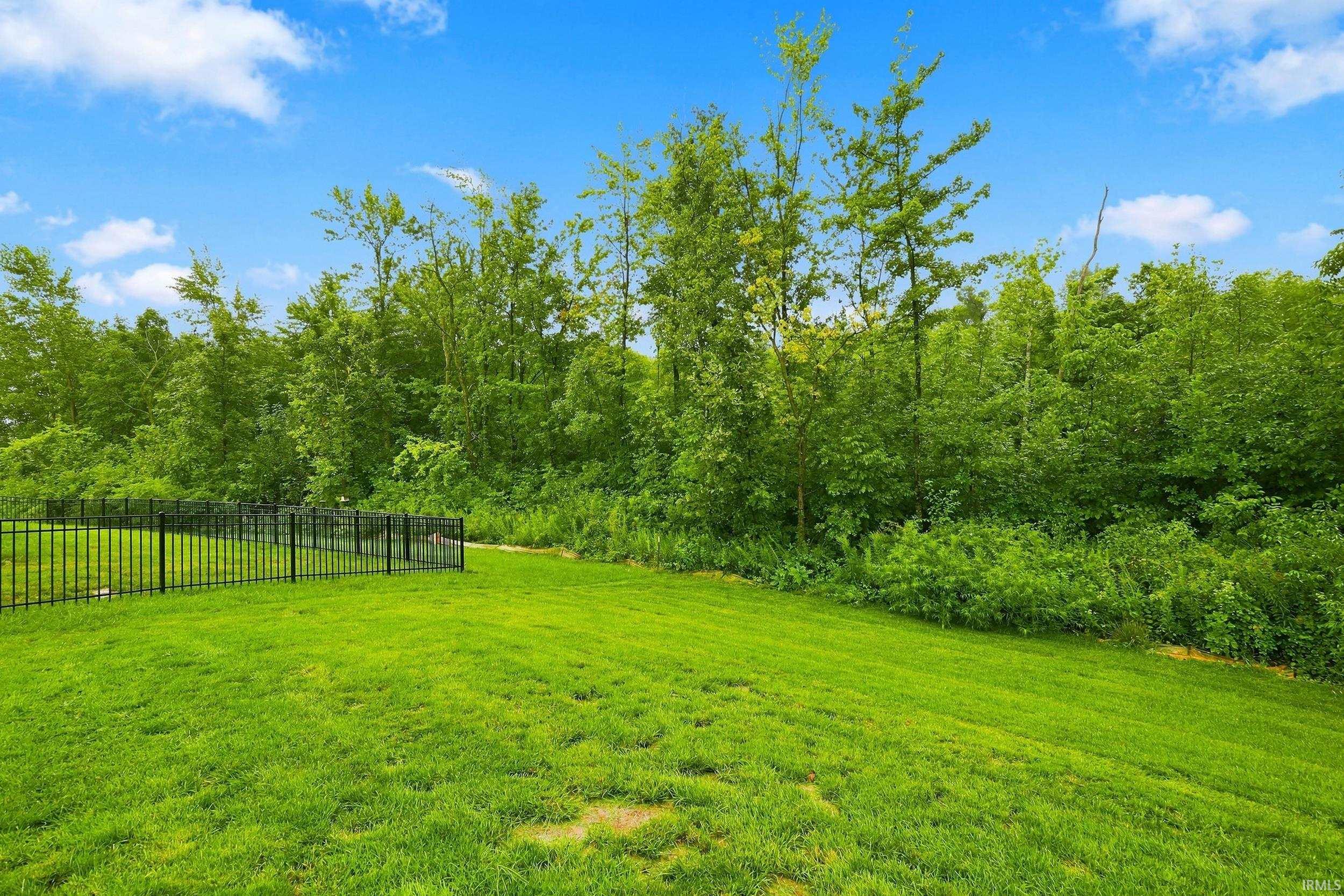 Expansive green lawn with a black metal fence and mature trees