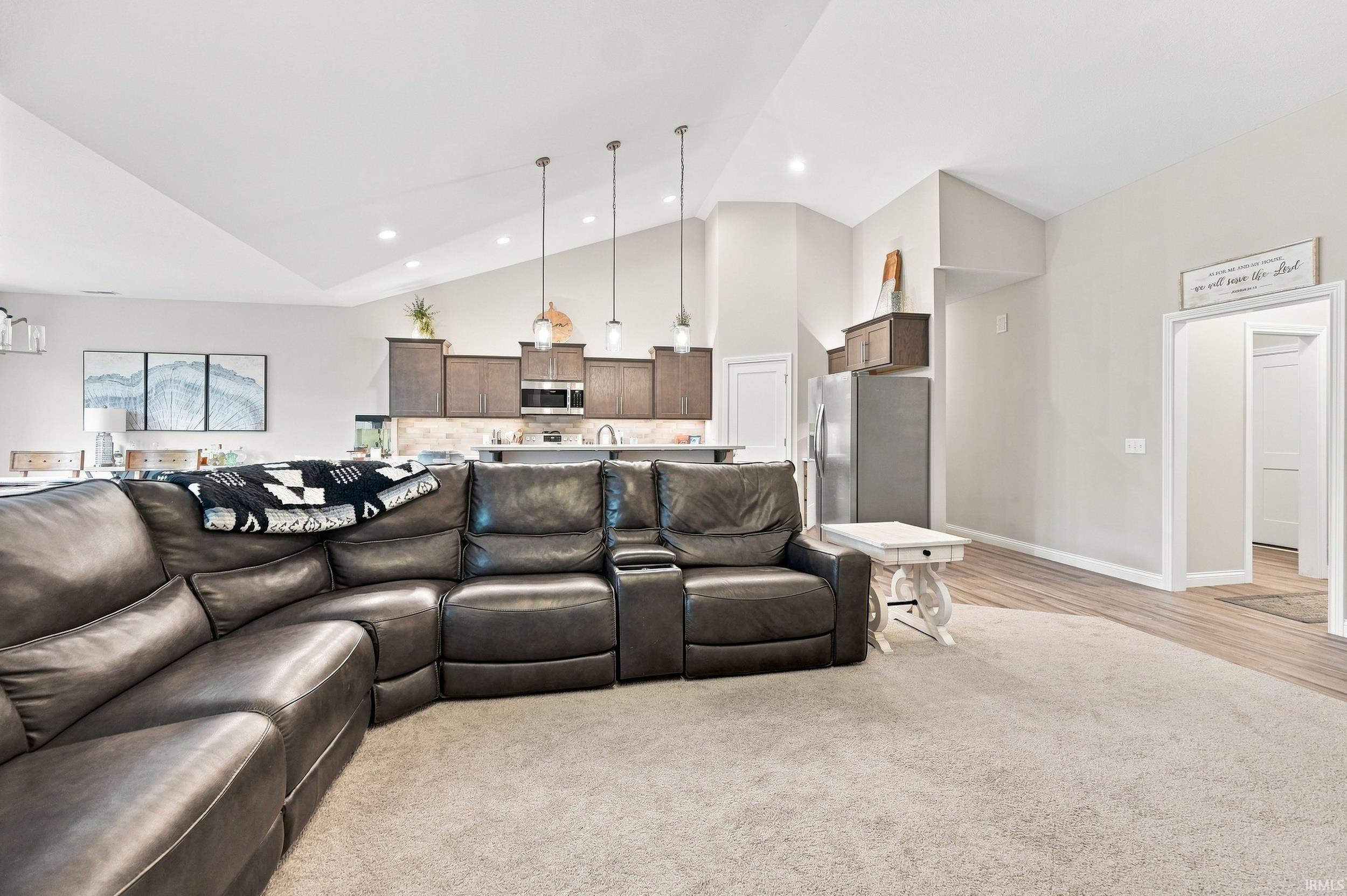 Vaulted ceilings with recessed lighting, brown cabinetry, stainless steel appliances, pendant lighting, and wood-finish flooring