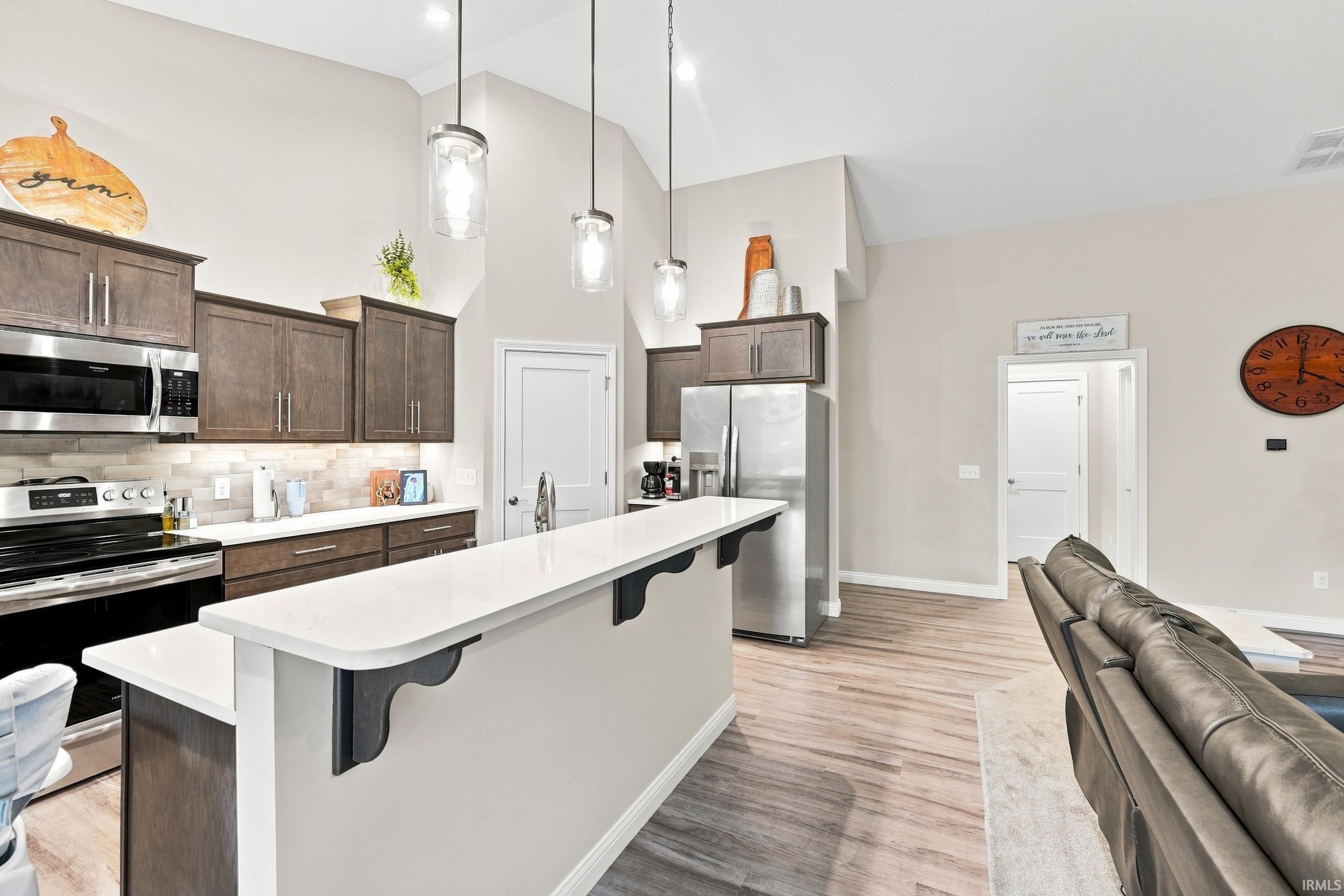 Kitchen featuring stainless steel appliances, wood-finish cabinetry, quartz countertops, and a tile backsplash