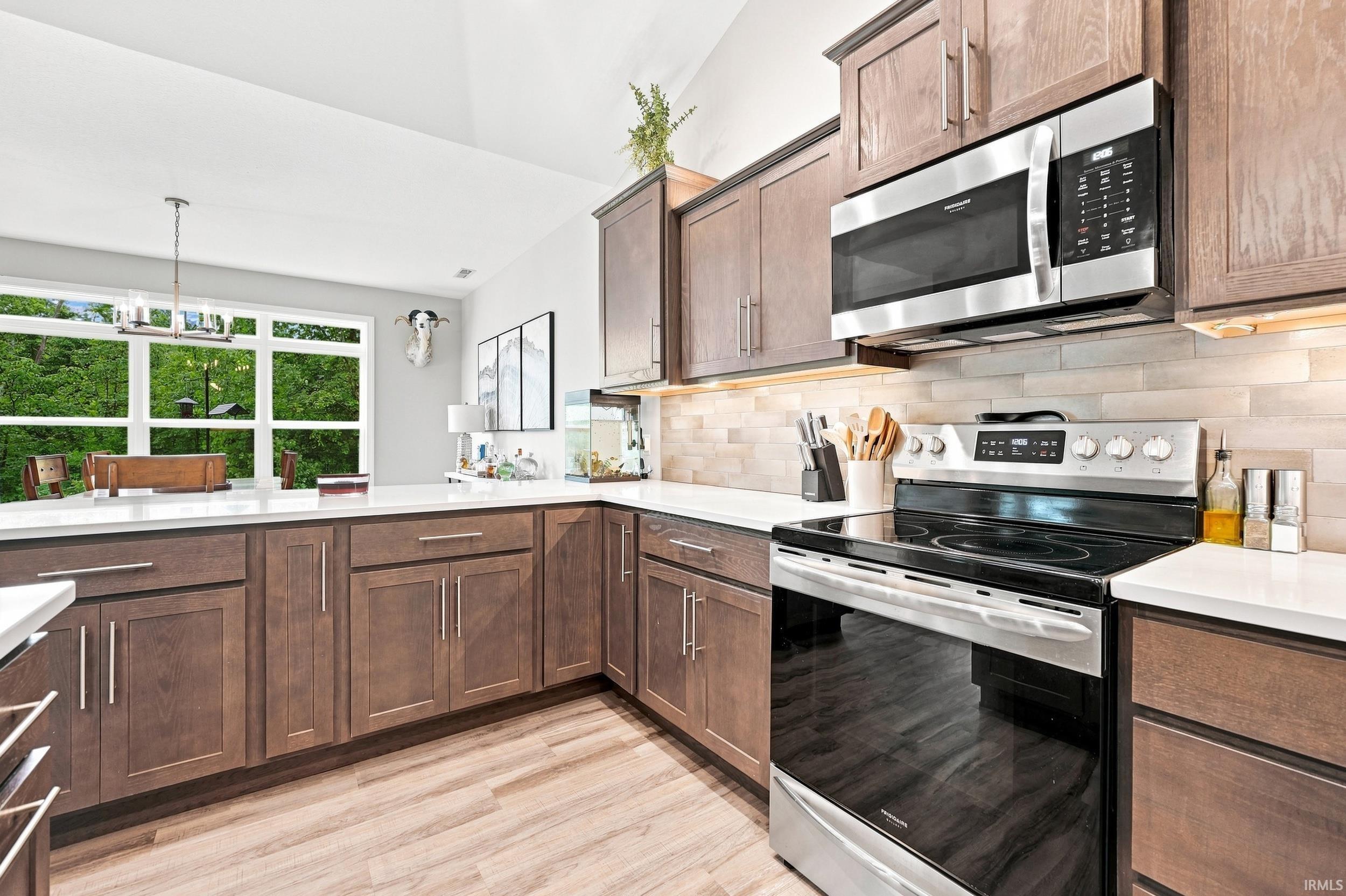 Contemporary kitchen featuring wood-finish cabinetry, white countertops, a mosaic tile backsplash, and stainless steel appliances