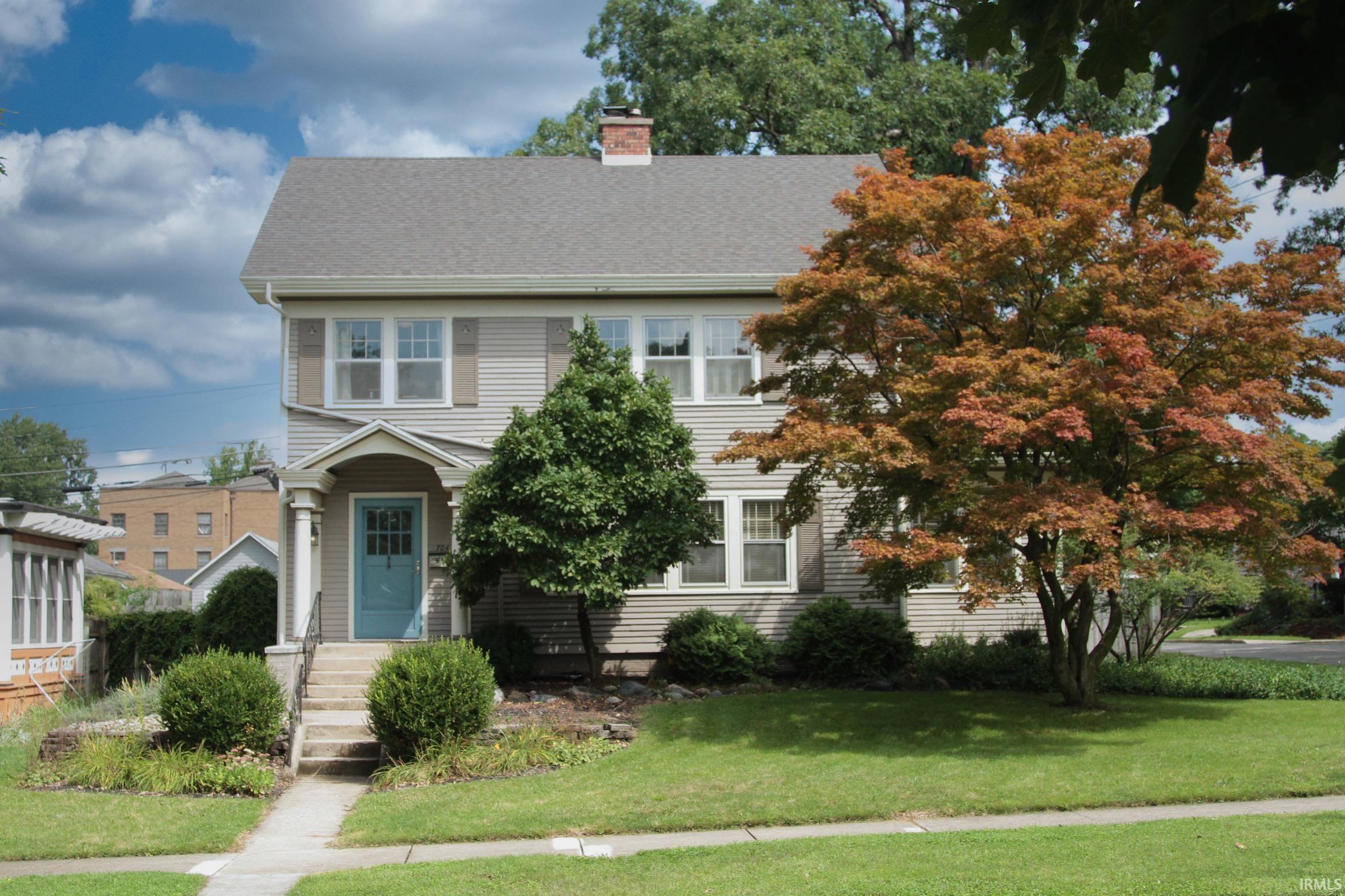 Two-story residence with a light gray siding exterior, featuring a covered front entry with columns and a contrasting blue door