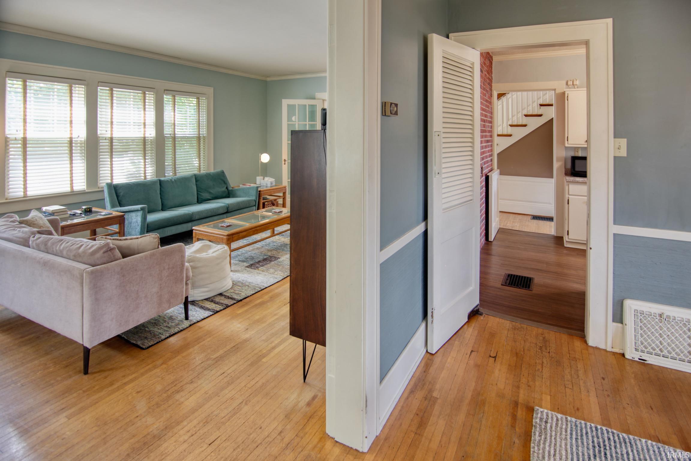 Hardwood flooring throughout, multiple windows with blinds, white trim, and a white louvered door