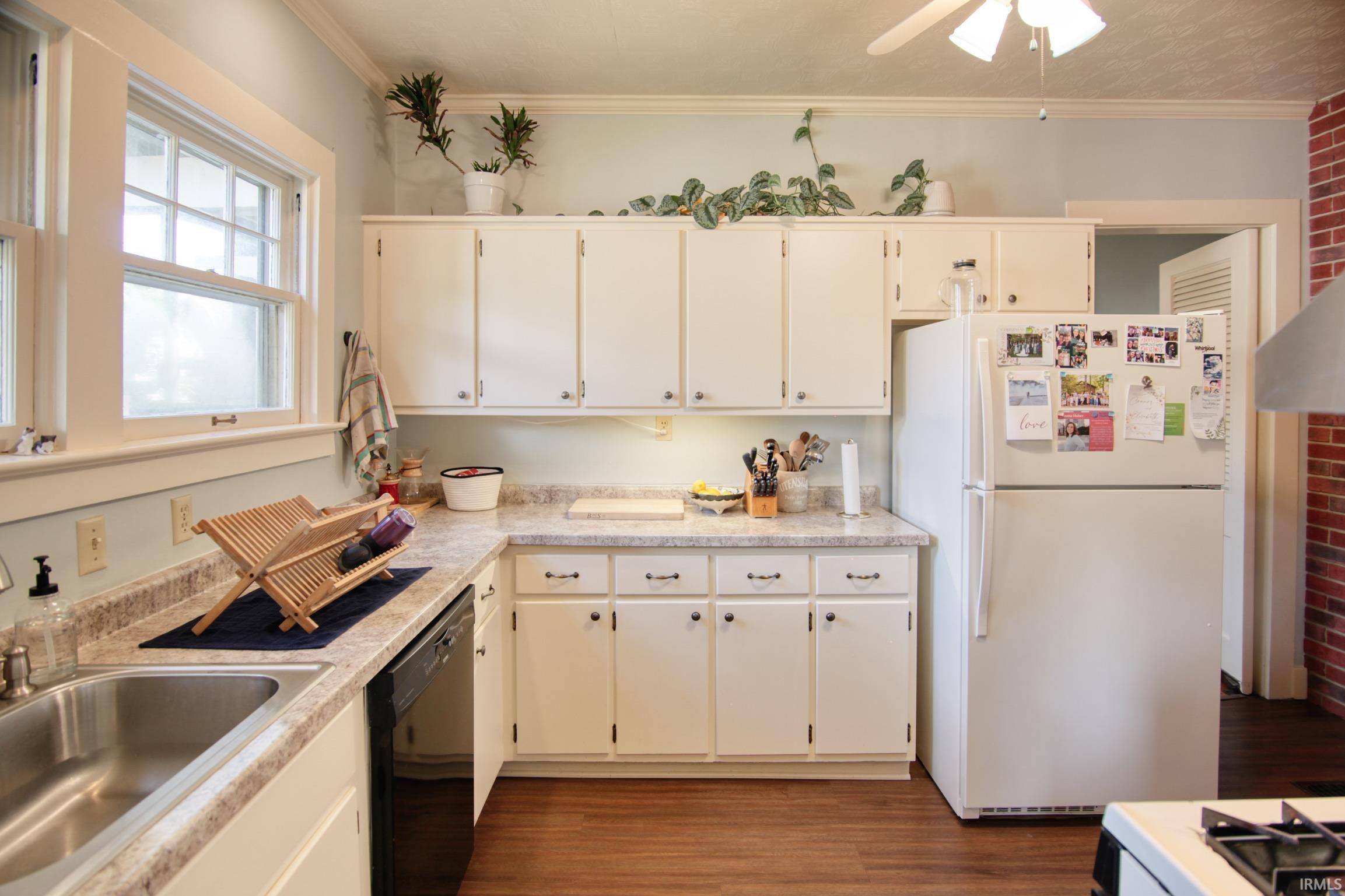 Kitchen featuring white cabinetry, light-toned countertops, wood-finish flooring, a stainless steel sink, and a double-hung window