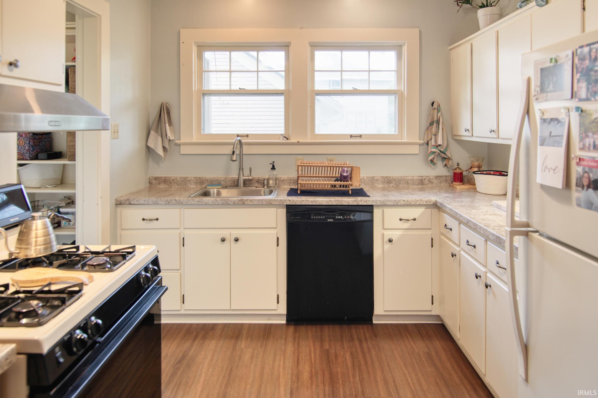 Kitchen featuring wood-finish flooring, white cabinetry, a double basin sink, and a dishwasher