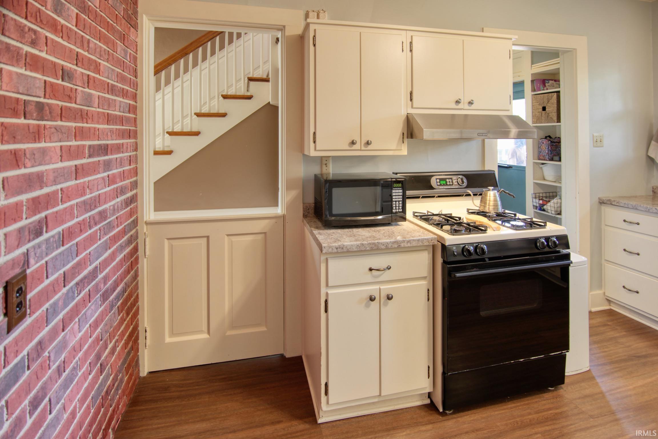 Kitchen featuring wood-finish flooring, white cabinetry, a black range, and a stainless steel range hood