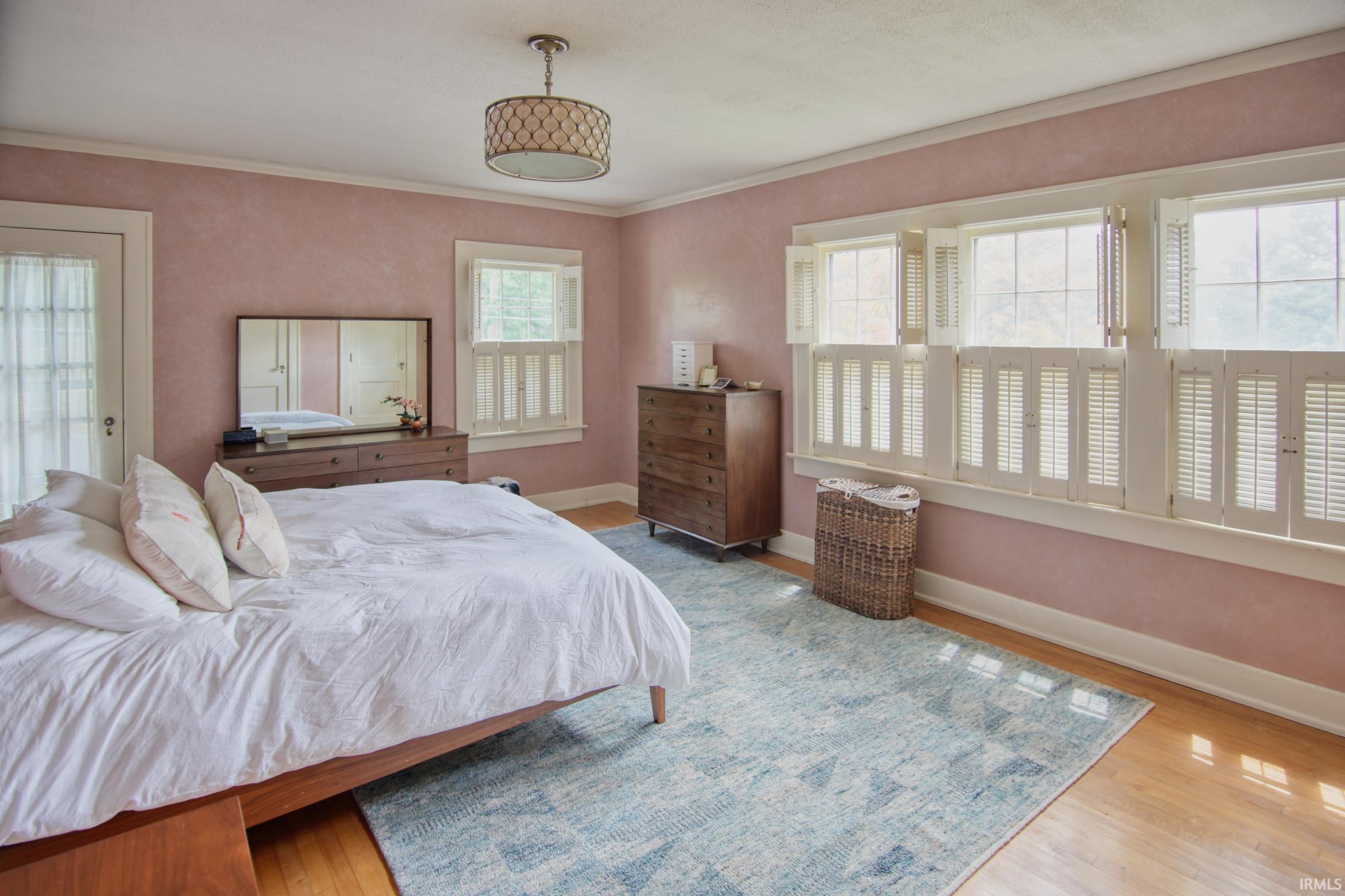 Hardwood flooring, multiple windows with plantation shutters, ceiling-mounted light fixture, and a glass-paneled door