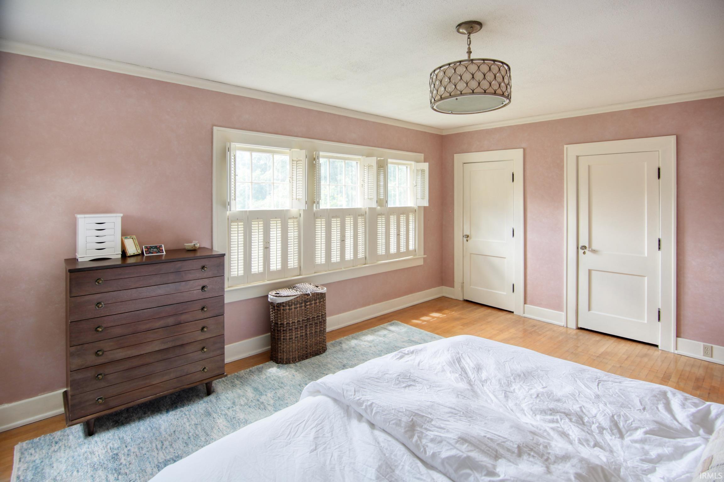 Hardwood flooring, two panel doors, window with plantation shutters, and a decorative ceiling fixture