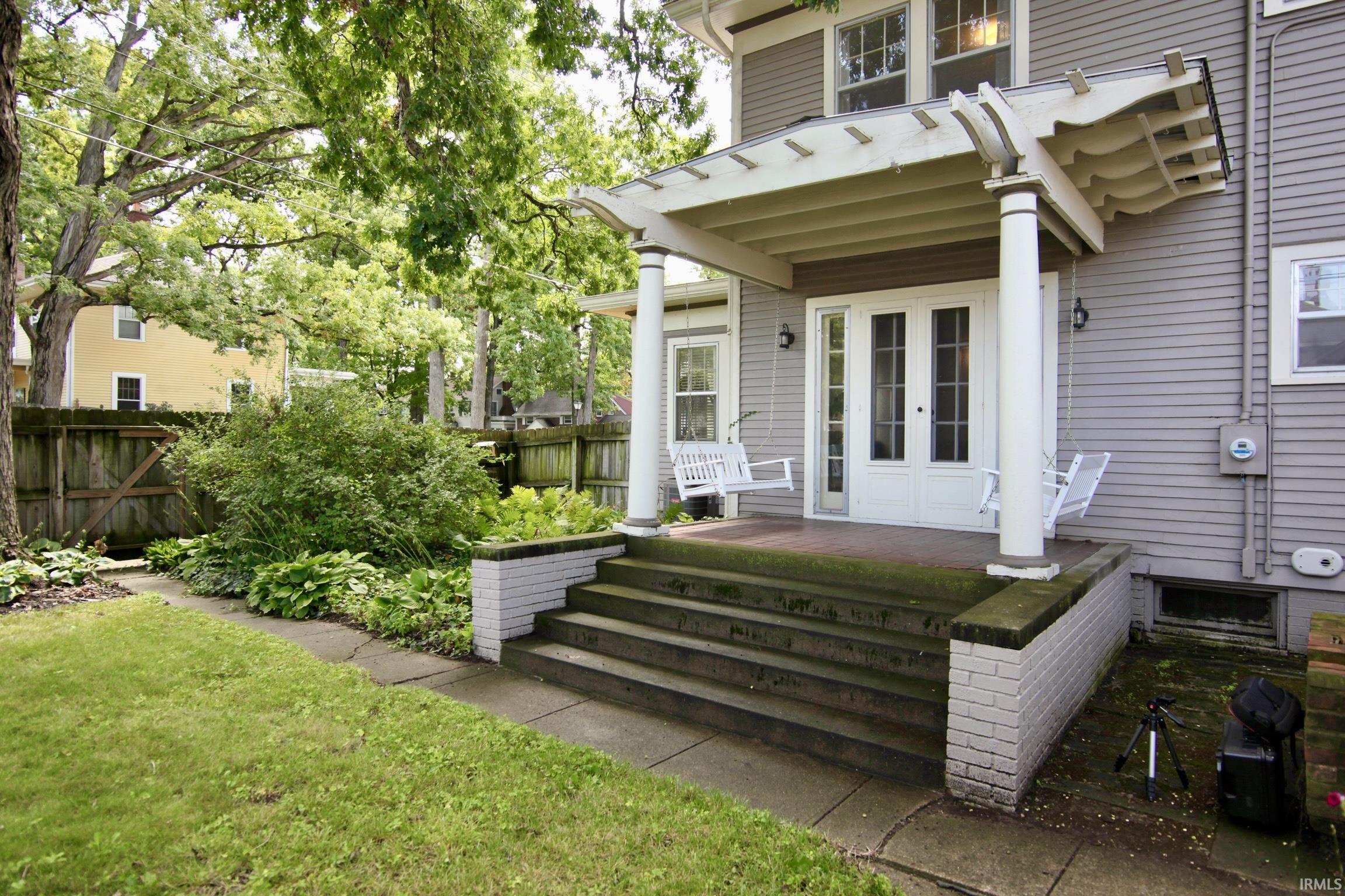 Covered porch with swings, white columns, wood siding exterior, and wood fencing