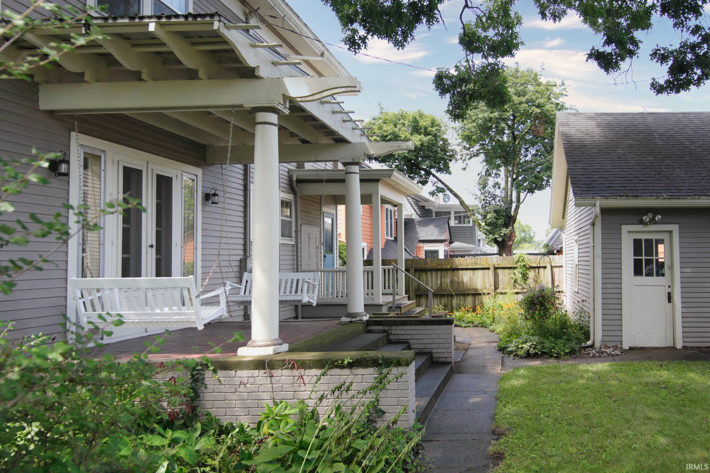 Expansive side porch with pergola, multiple entry points, brick foundation, and concrete steps
