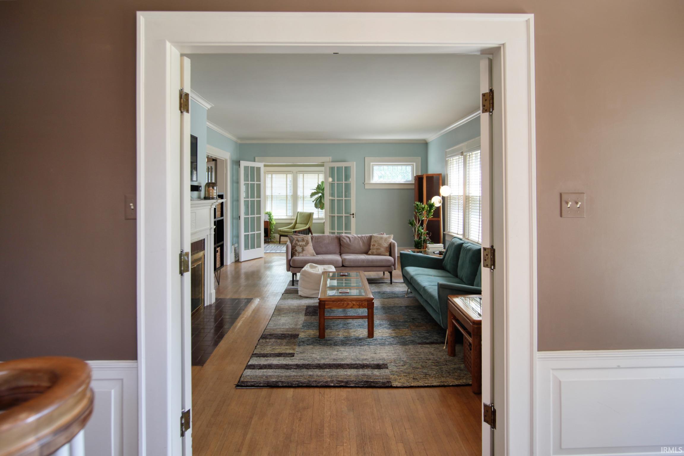 Hardwood flooring, white crown molding, white wainscoting, and a fireplace with a white mantel