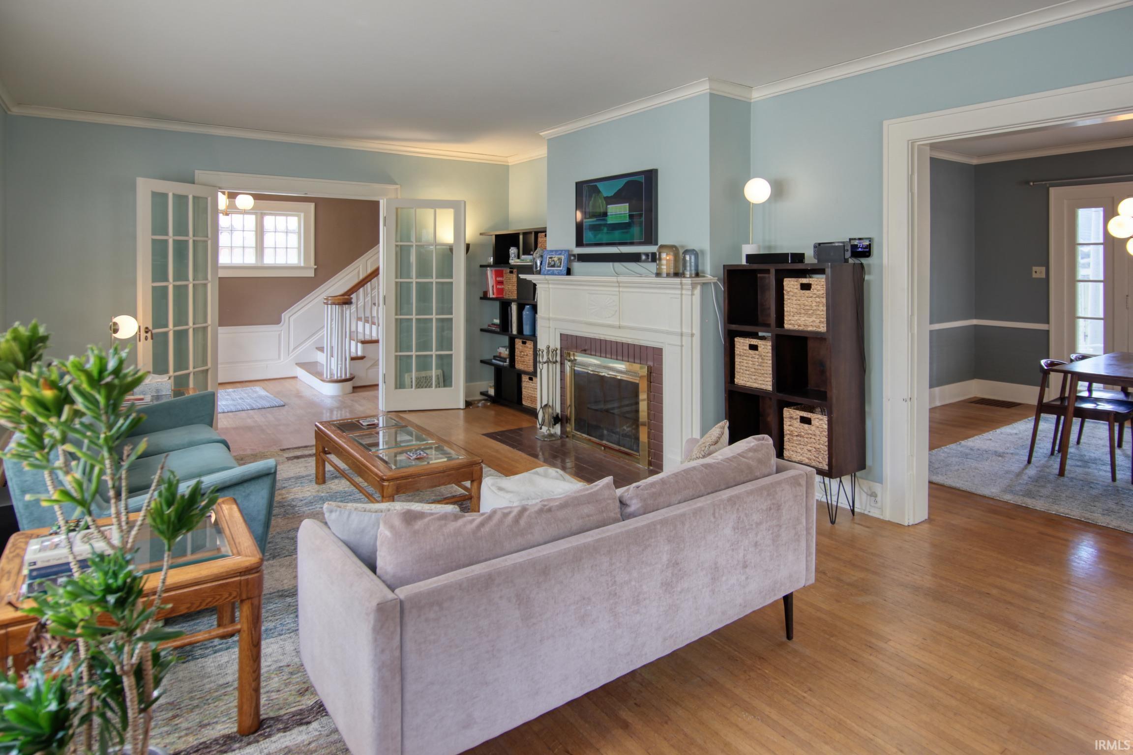 Hardwood flooring, white crown molding, fireplace with white mantel, French doors, and built-in shelving