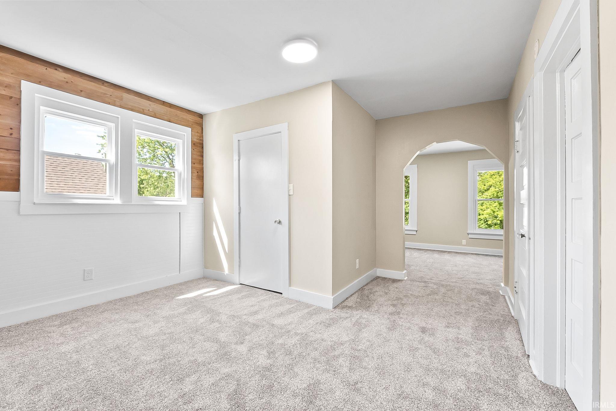 Plush gray carpeting throughout, arched entryway, white trim, dual pane windows, and a wood-paneled accent wall