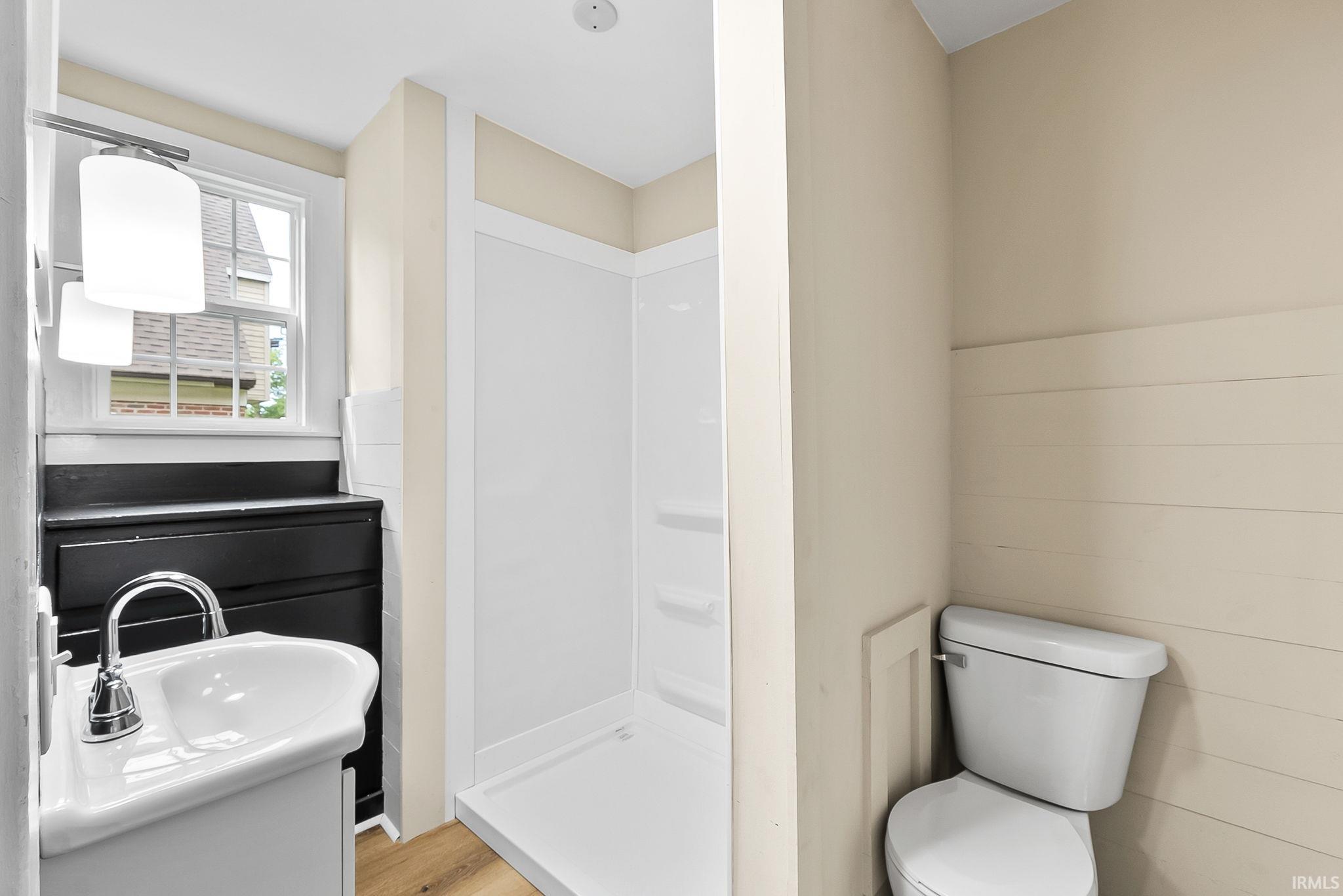 Compact bathroom featuring a shower stall, pedestal sink, chrome fixtures, and a window