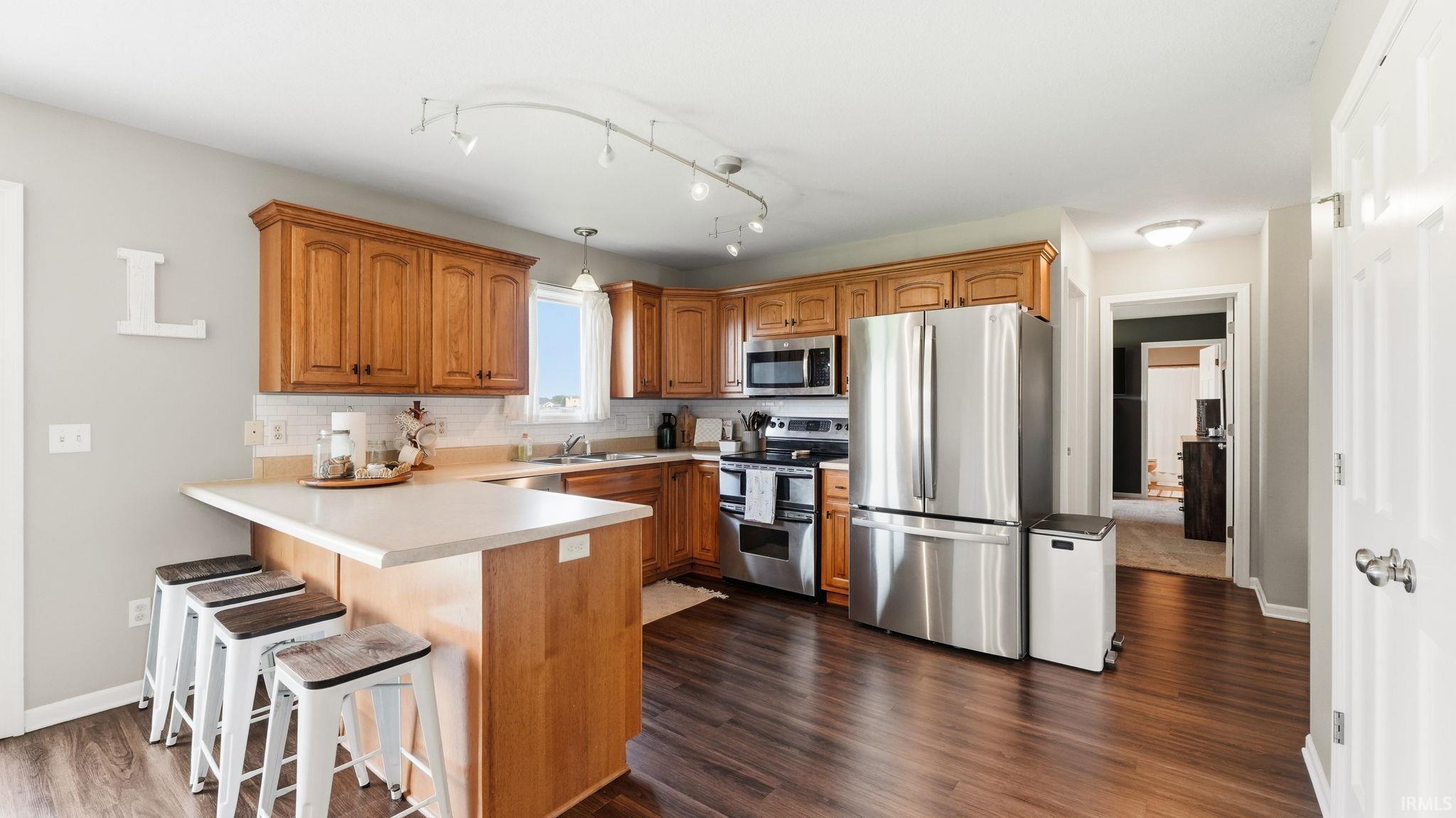 Wood-finish flooring, wood cabinetry, light countertops, subway tile backsplash, and stainless steel appliances