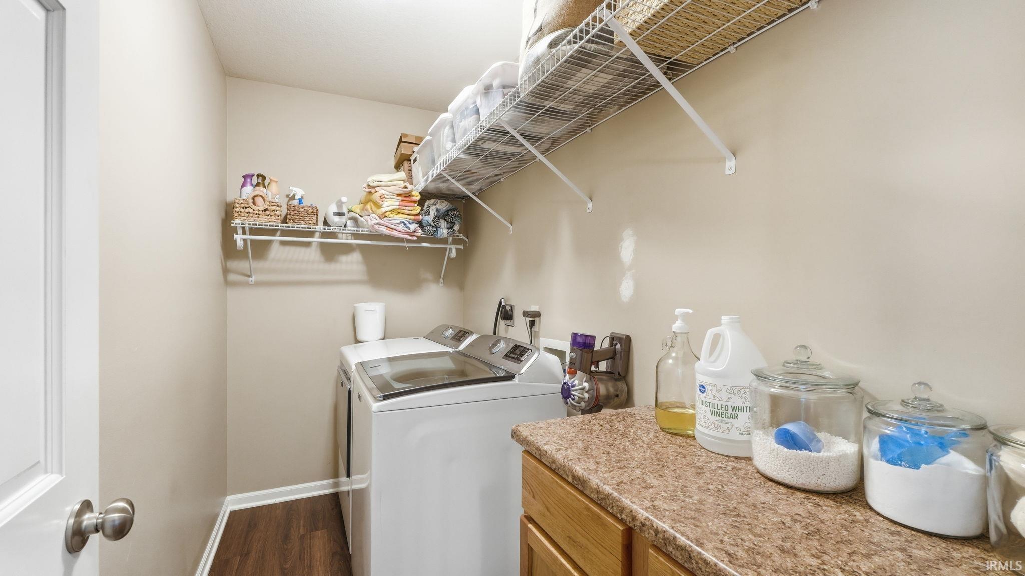 Laundry area featuring wood-finish flooring, two wall-mounted wire shelving units, and a built-in counter with wood cabinetry