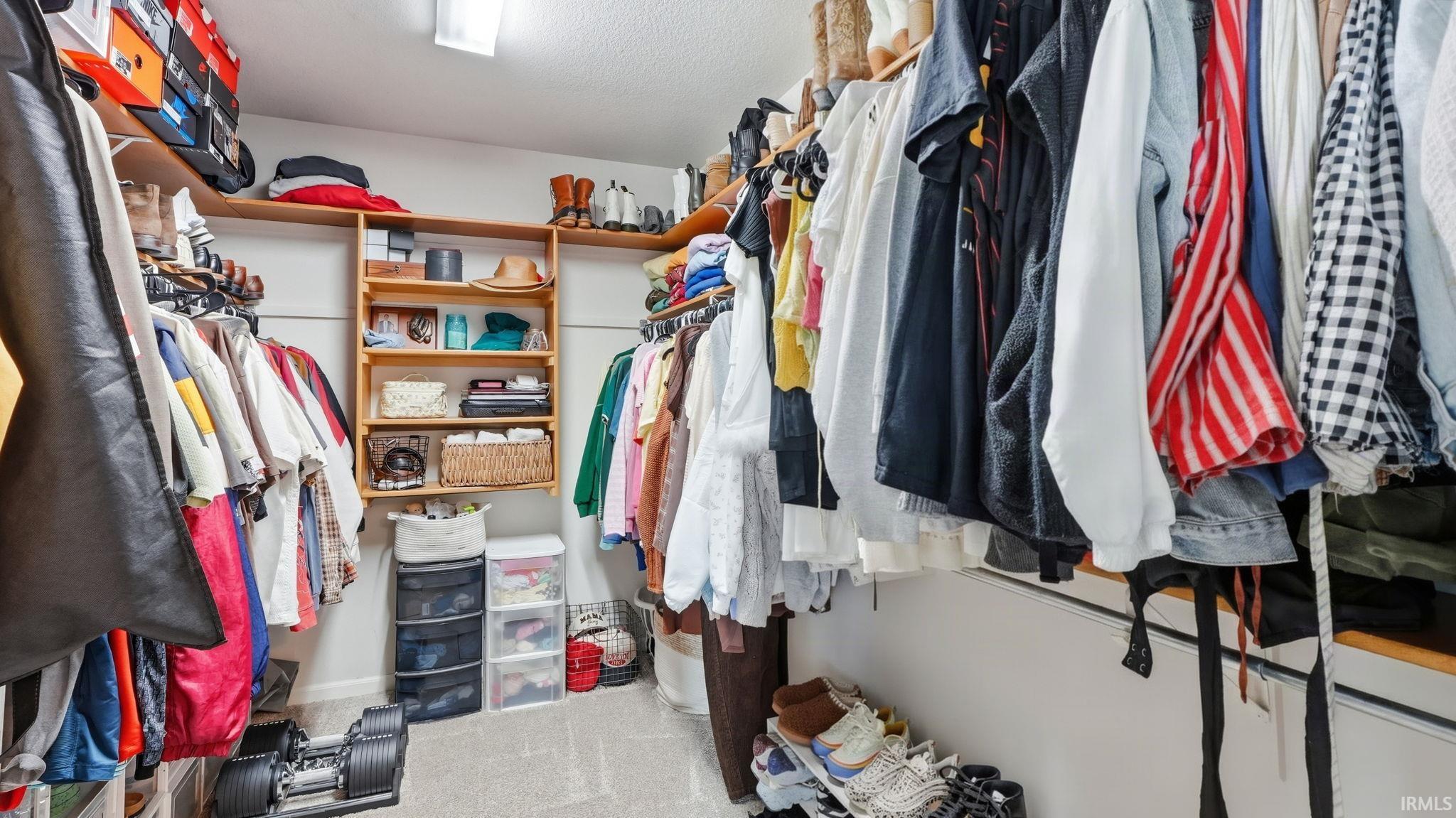 Recessed ceiling lighting illuminates a walk-in closet featuring built-in wood shelving and multiple hanging rods