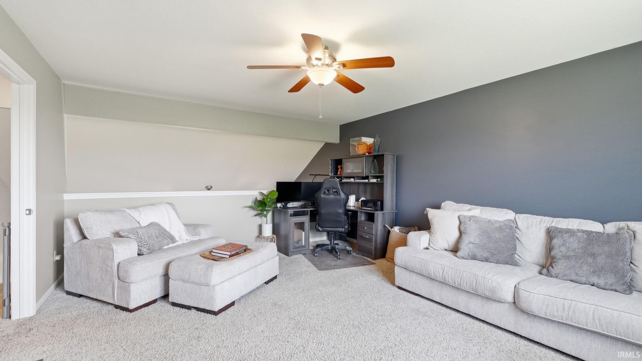 Carpeted area with a ceiling fan, a contrasting accent wall, and built-in shelving