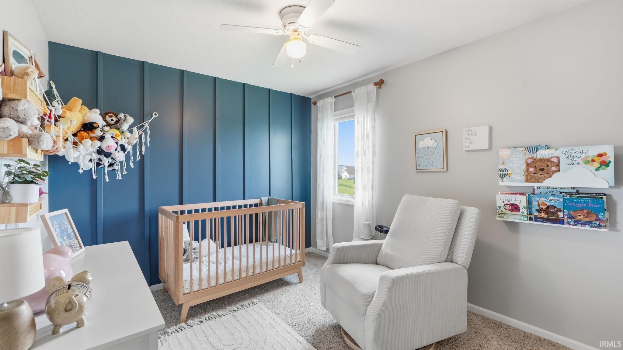 Accent wall with vertical paneling, ceiling fan with light fixture, window with white trim, wall-mounted shelving, and carpeted flooring