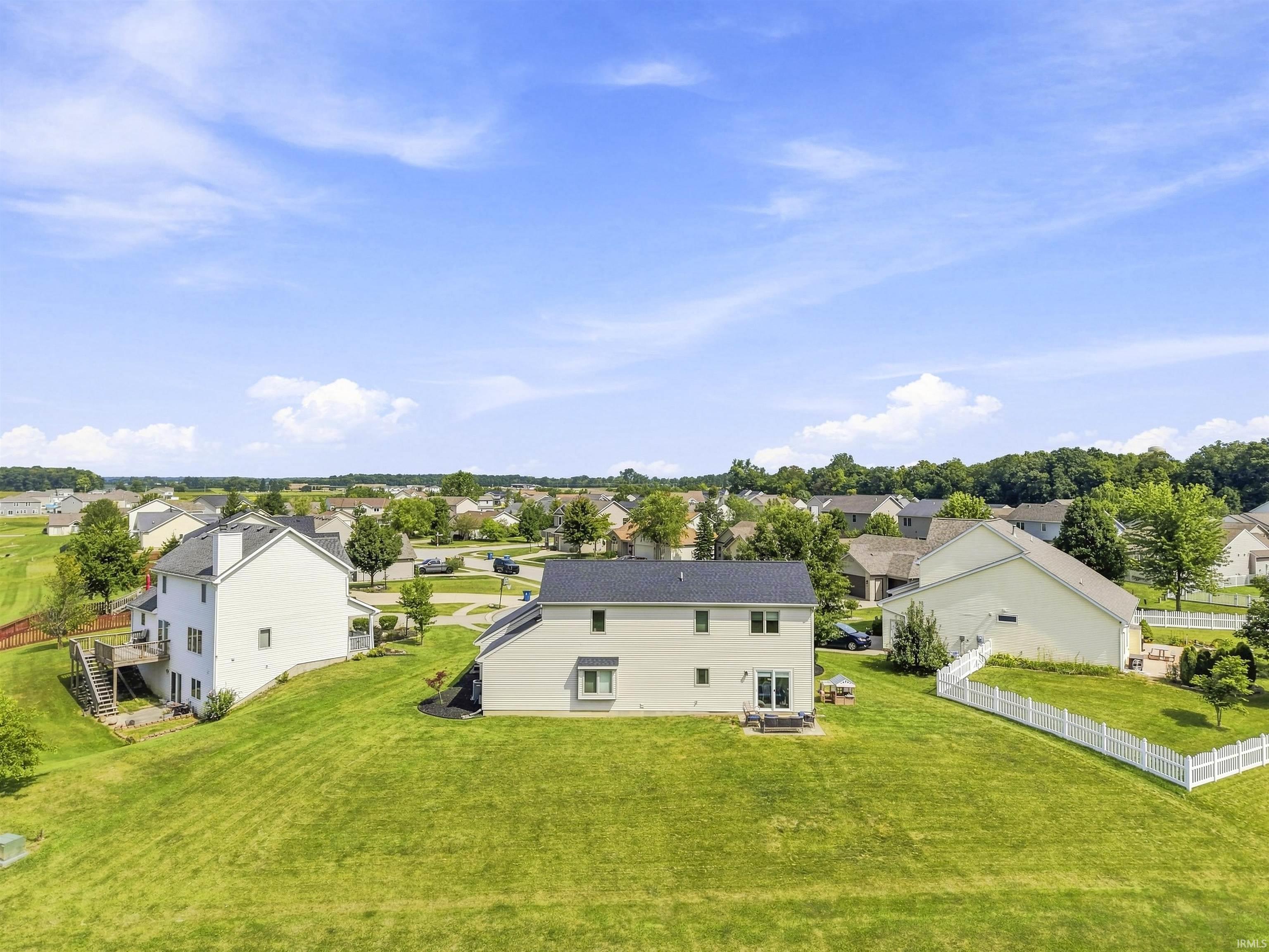Expansive green space with a sloping terrain, featuring a white vinyl fence
