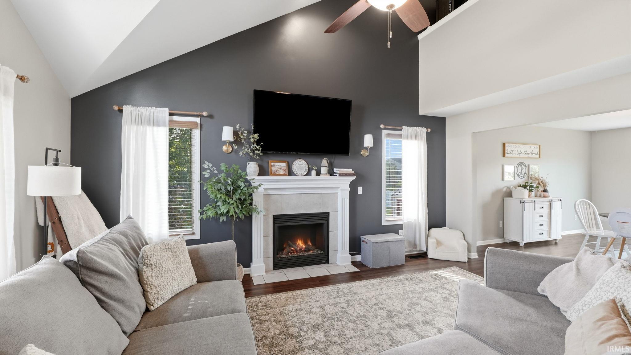 Vaulted ceiling with a ceiling fan, fireplace with a tile surround and mantel, wood-finish flooring, and wall sconces