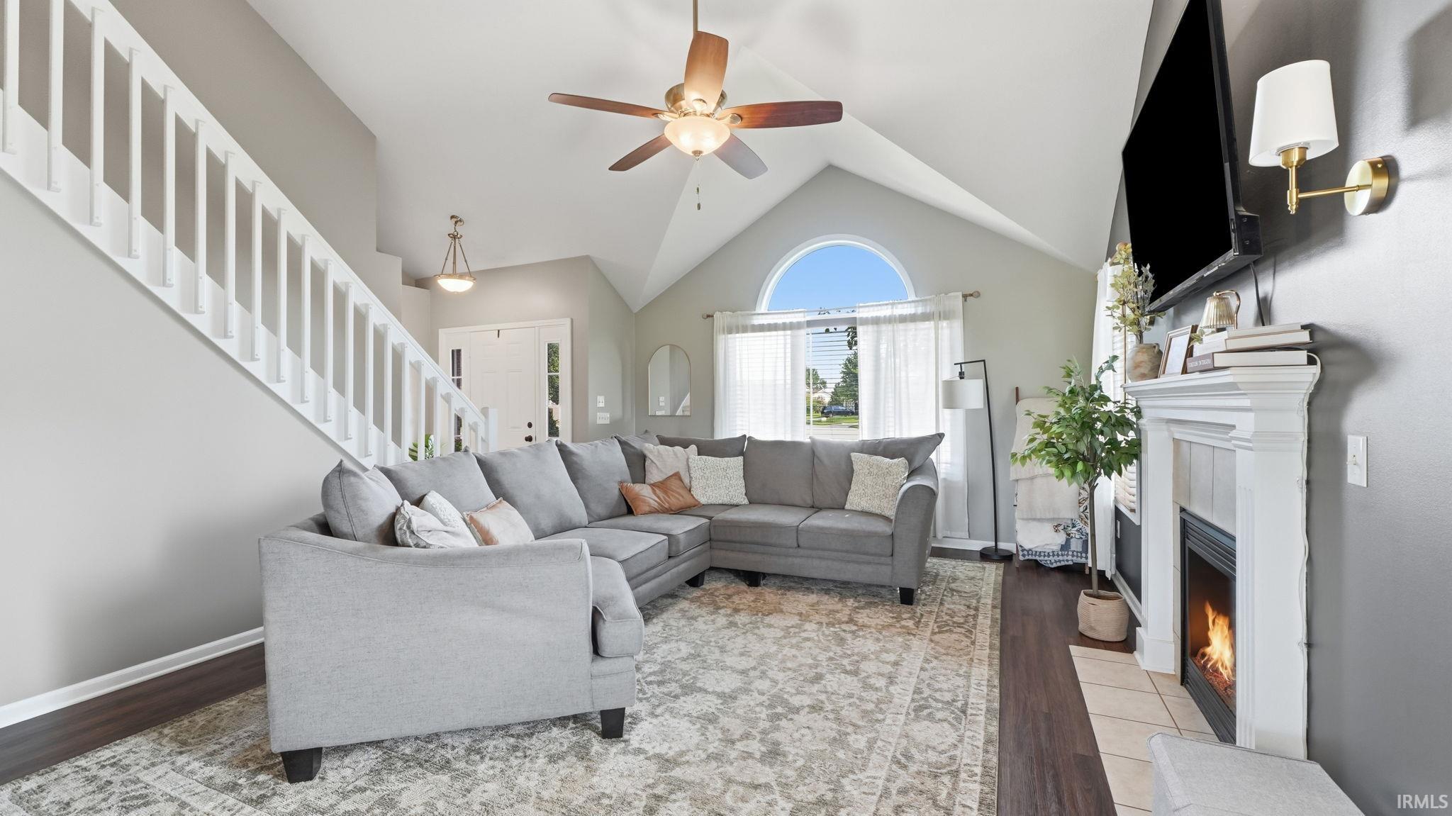 Vaulted ceiling with a ceiling fan, arched window, white fireplace with a mantel, and dark wood-finish flooring