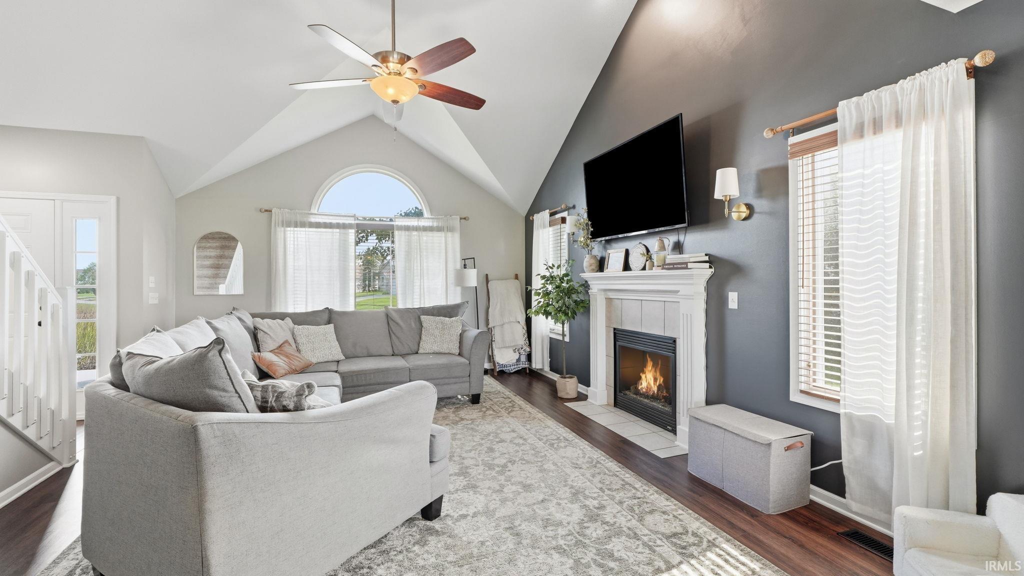Wood-finish flooring, vaulted ceiling, arched window, built-in fireplace, and ceiling fan with integrated lighting
