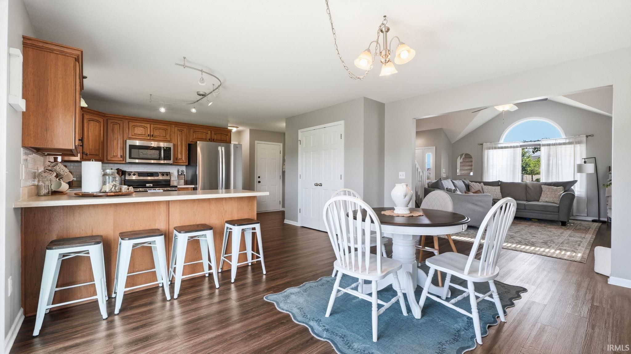 Wood-finish flooring throughout, kitchen with wood cabinetry, stainless steel appliances, and a breakfast bar
