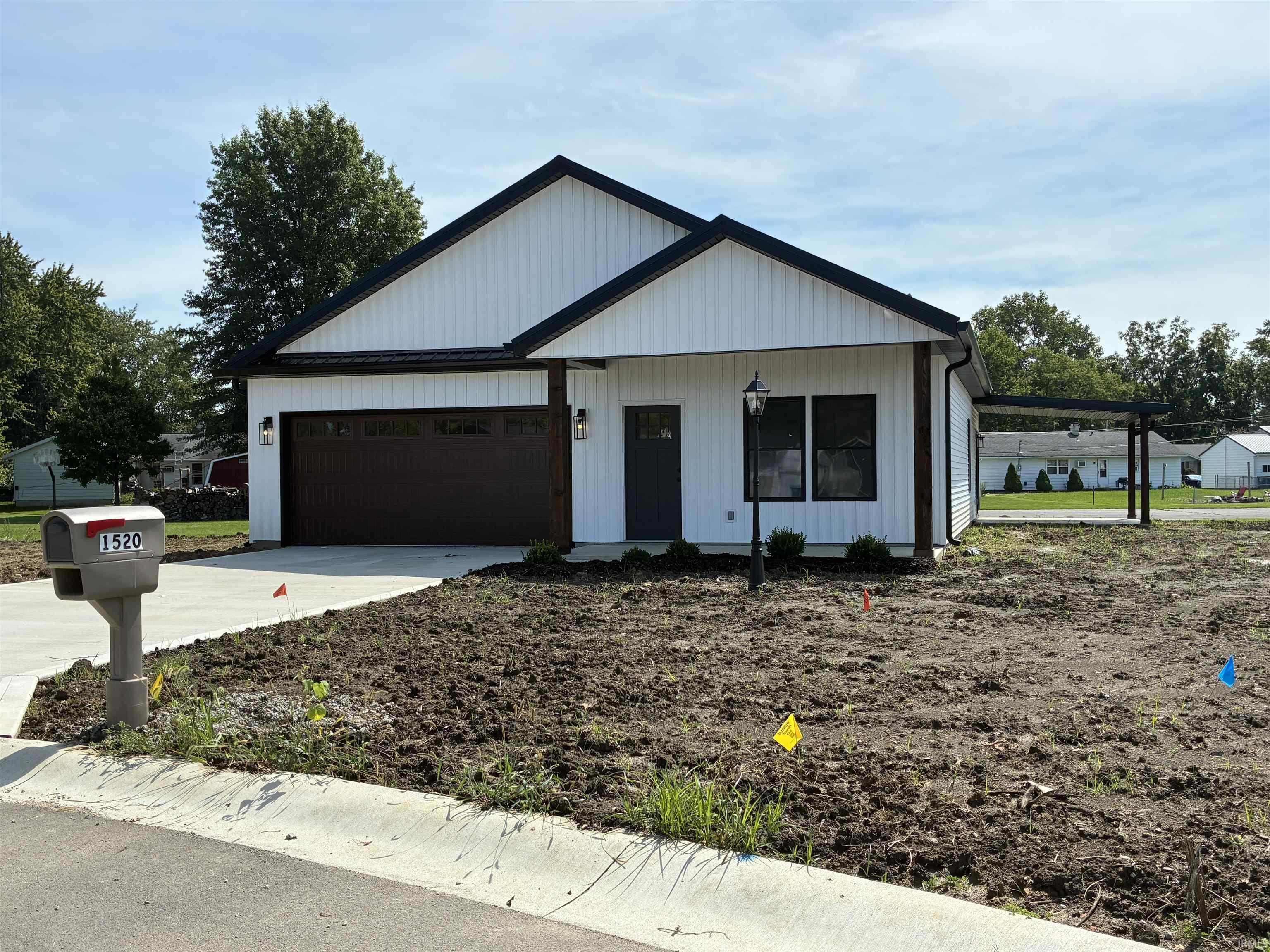 White vertical siding exterior with dark trim accents, attached carport, two-car garage, and concrete driveway