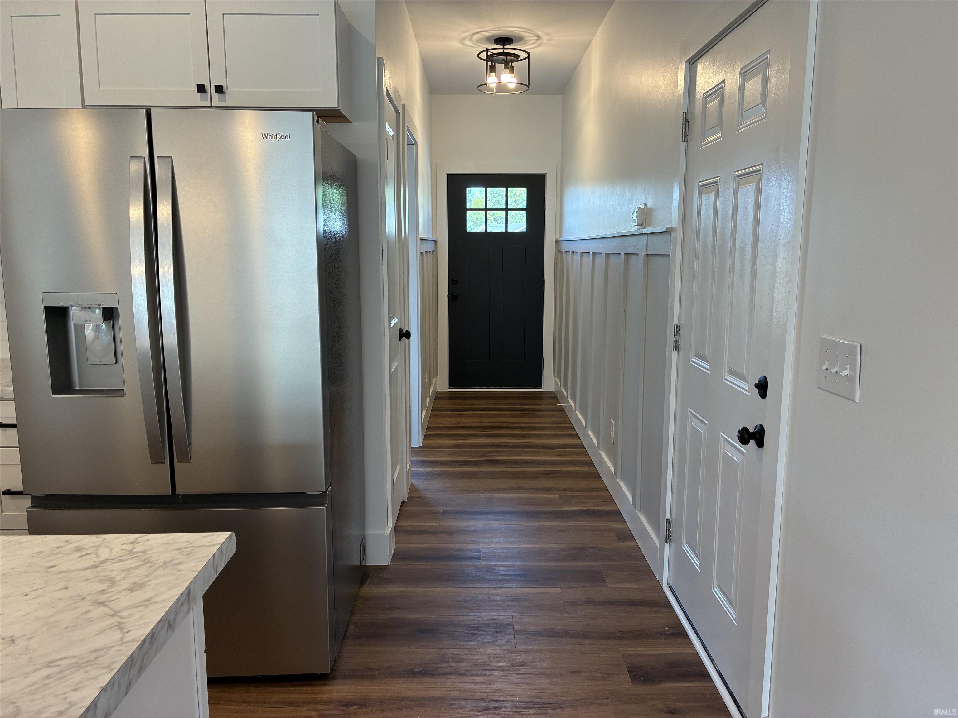 Wood-finish flooring, wainscoting detail, ceiling-mounted light fixture, paneled doors, and white cabinetry with dark hardware