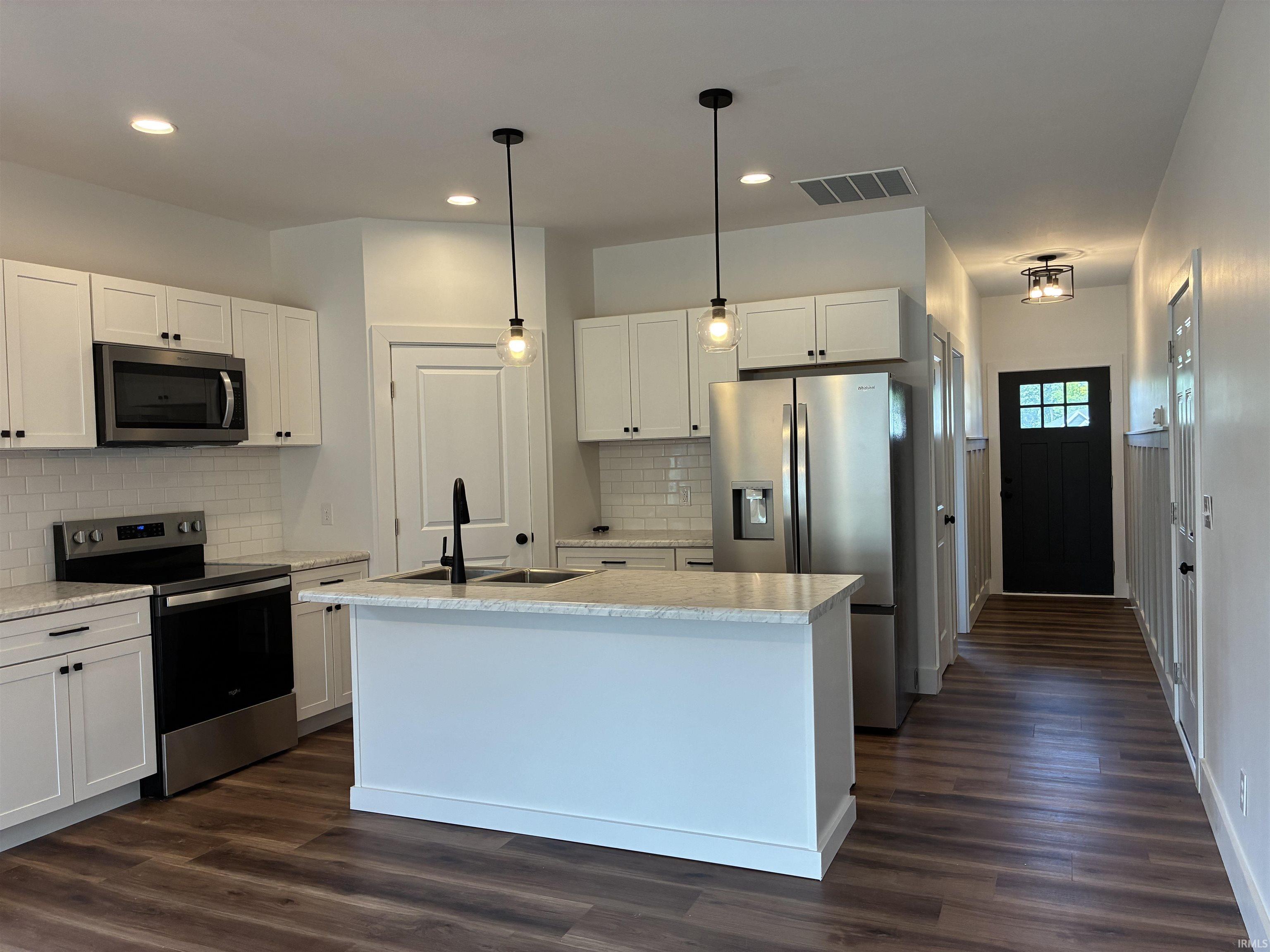 Modern kitchen featuring white shaker cabinetry, stainless steel appliances, a center island with sink, subway tile backsplash, and wood-finish flooring