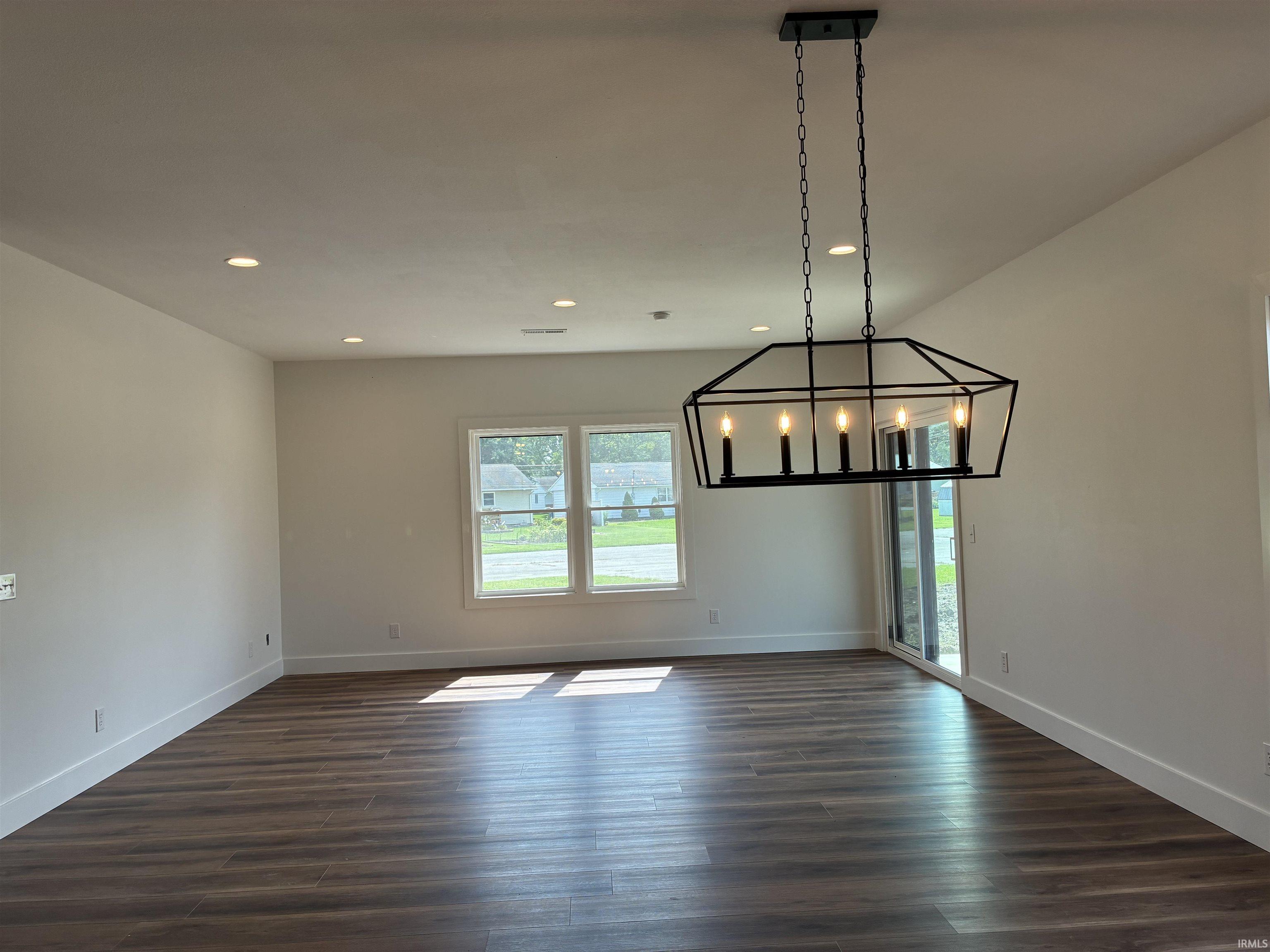 Recessed ceiling lighting, wood-finish flooring, geometric black chandelier, multiple windows, and sliding glass door