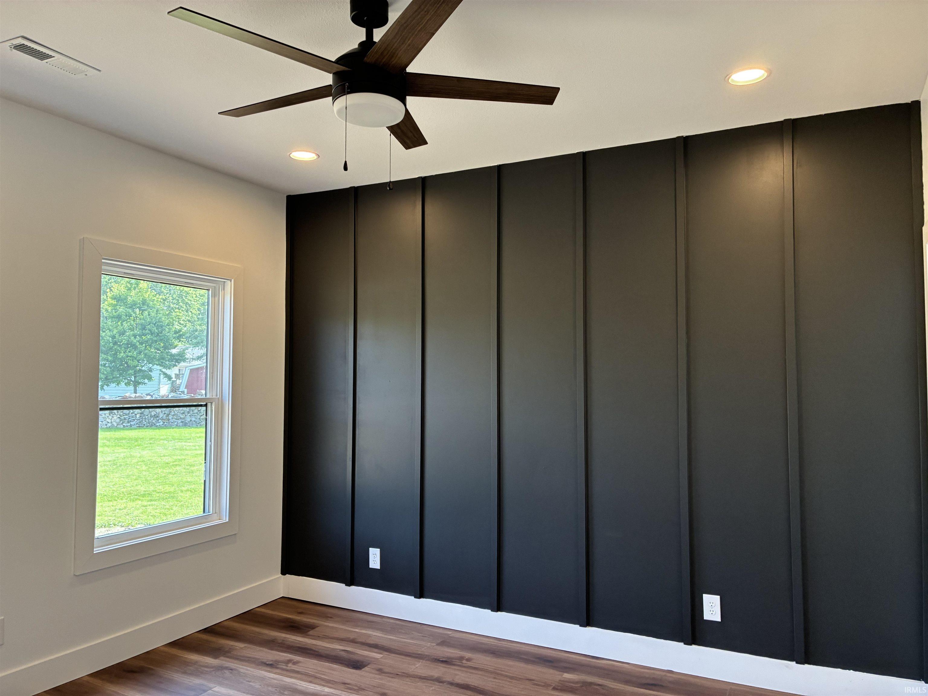Accent wall with vertical paneling, wood-finish flooring, recessed lighting, and a ceiling fan with light