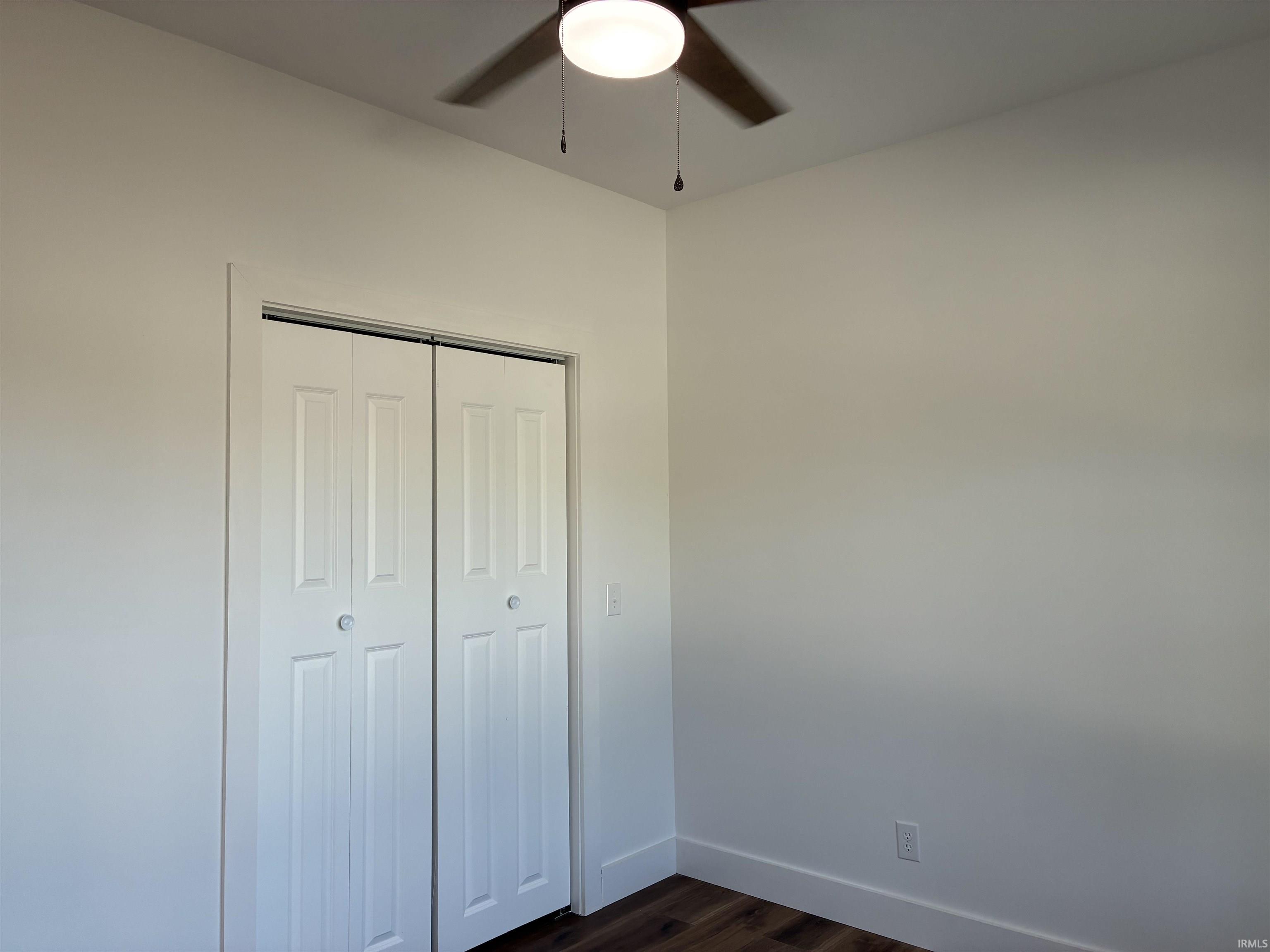 White bi-fold closet doors with round knobs, overhead ceiling fan with light fixture, and wood-finish flooring