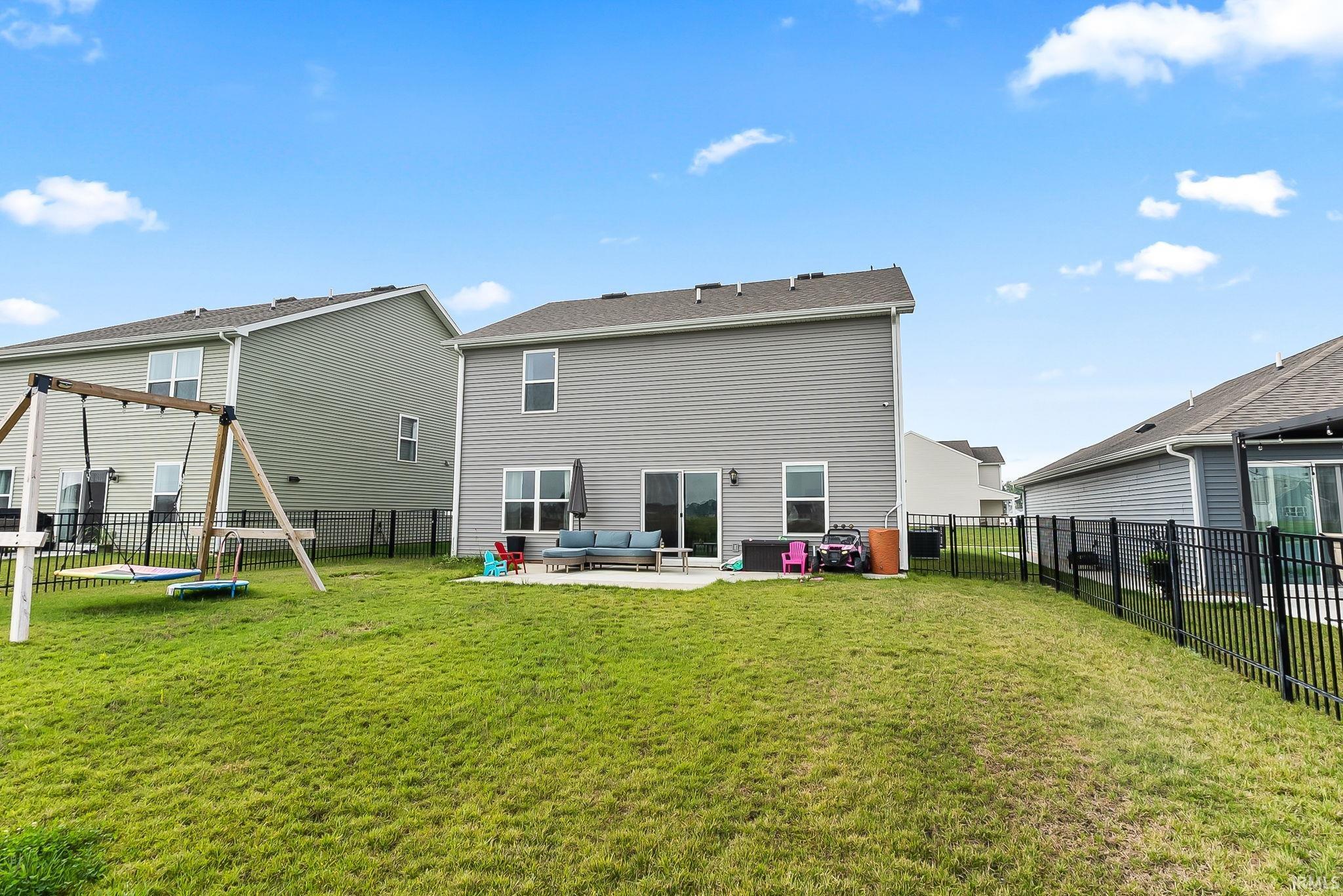 Expansive green lawn with a black metal fence, concrete patio, and a two-story exterior with siding